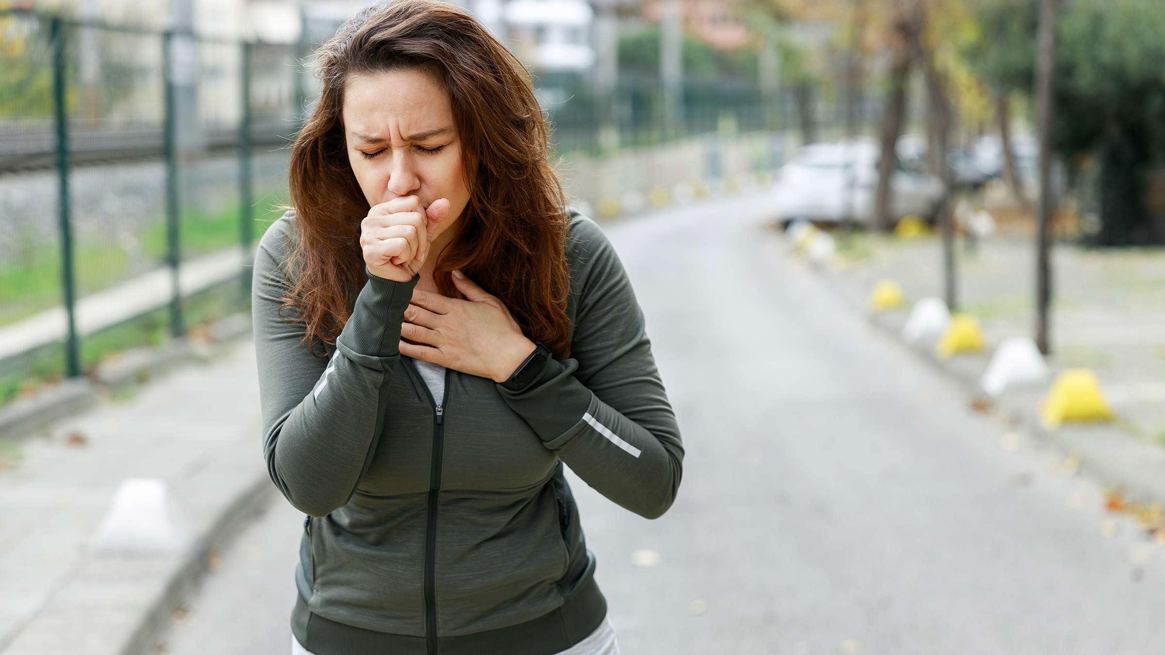 A young woman coughing while out exercising