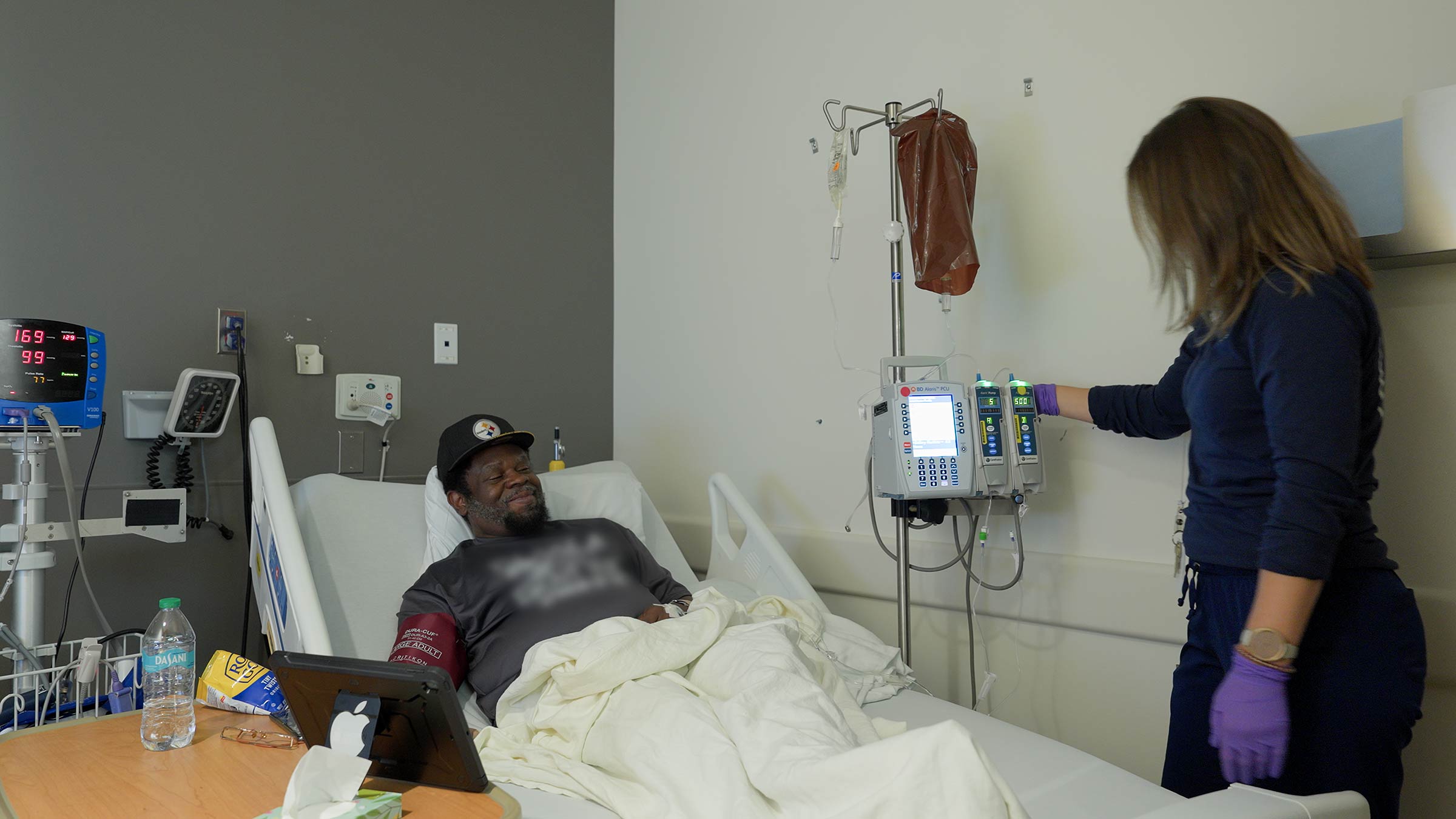 Madison Gregory IV lying in a hospital bed while a nurse is setting up the IV machine