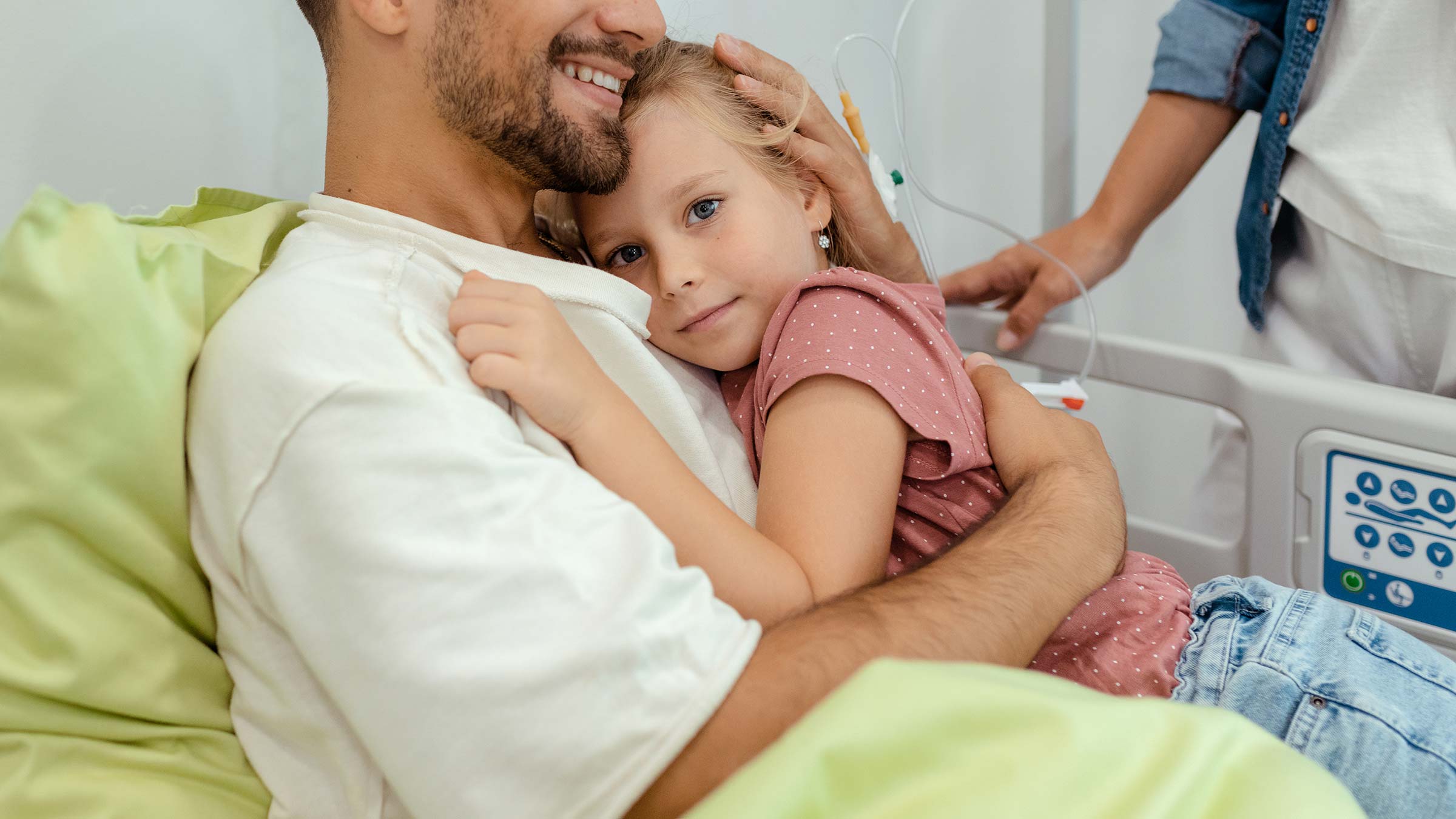 A male patient lying in a hospital bed hugging his child