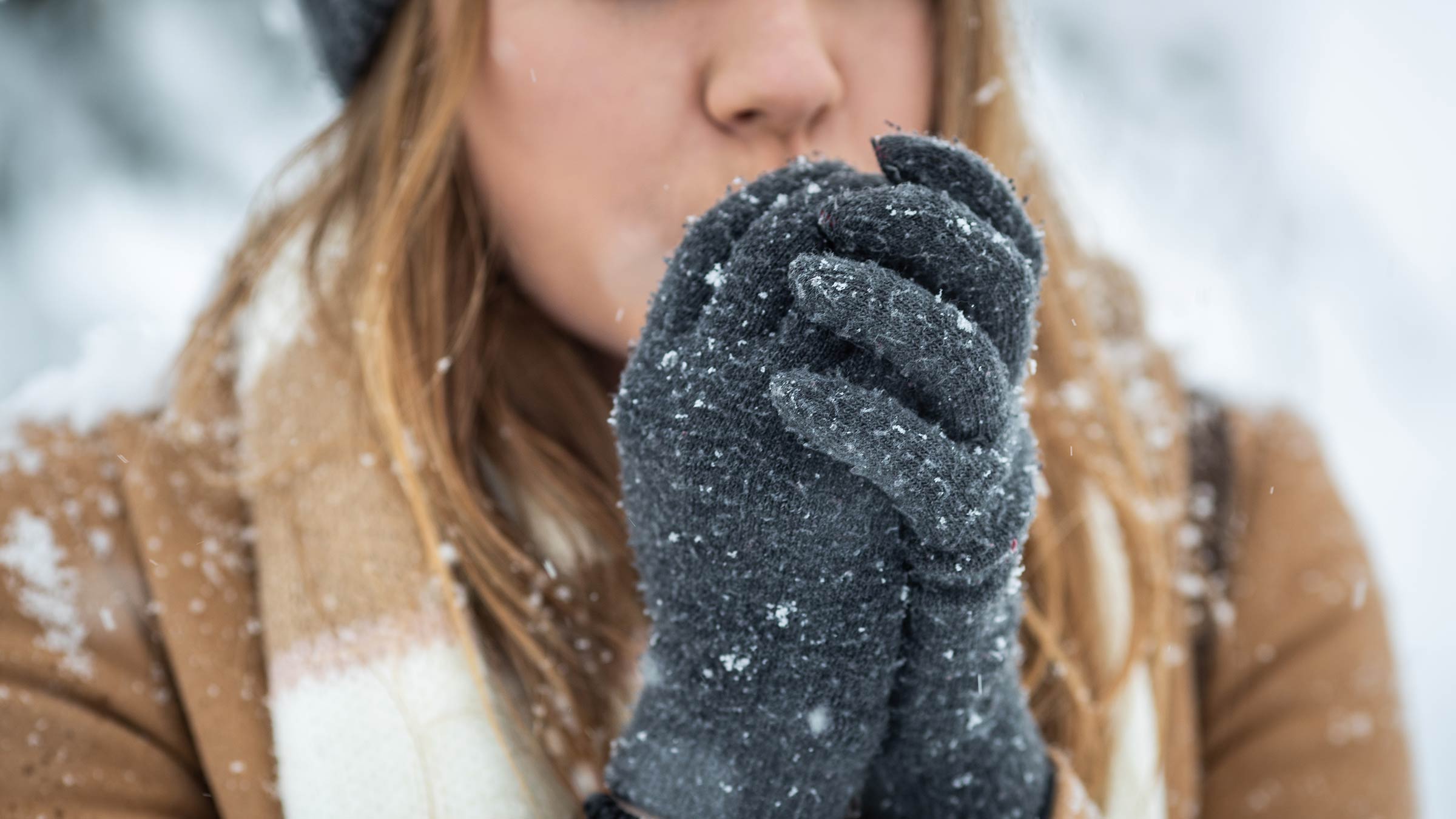 A woman blowing on her glove-covered hands to keep them warm