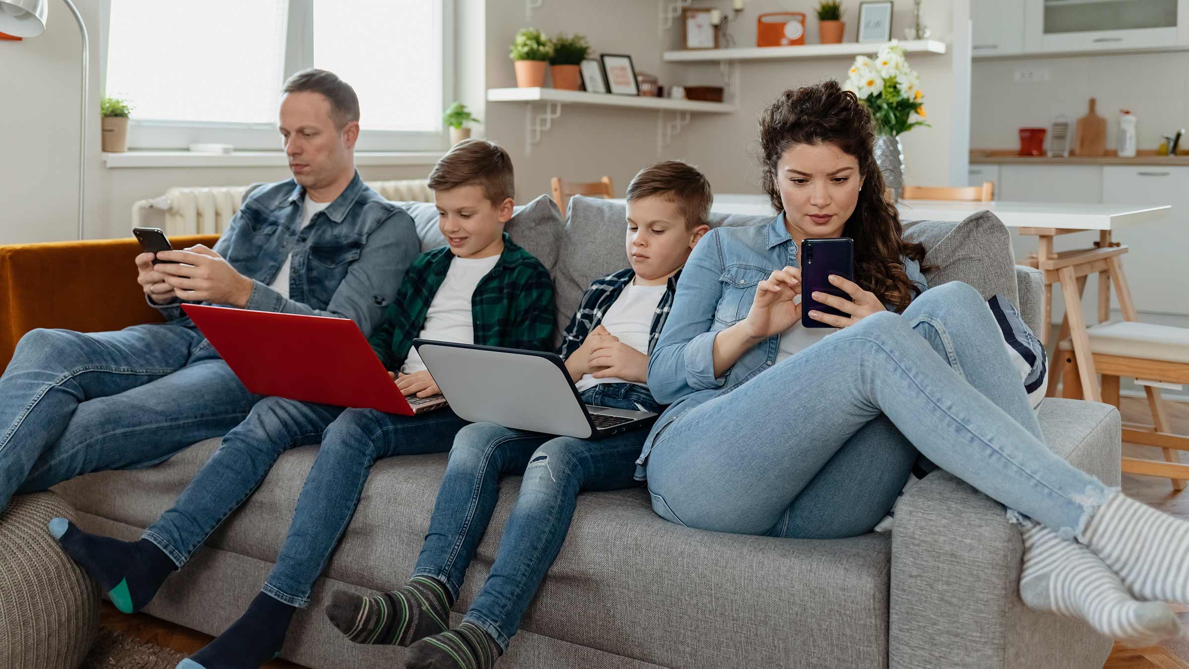 A family of four sitting in their living room, each using a digital device