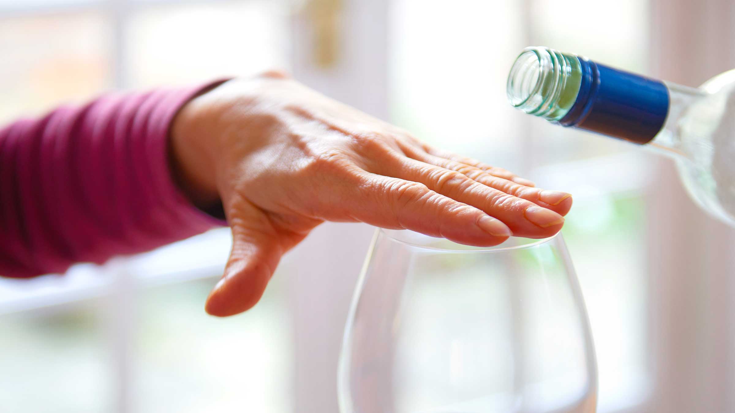 A person placing a hand over their empty wine glass