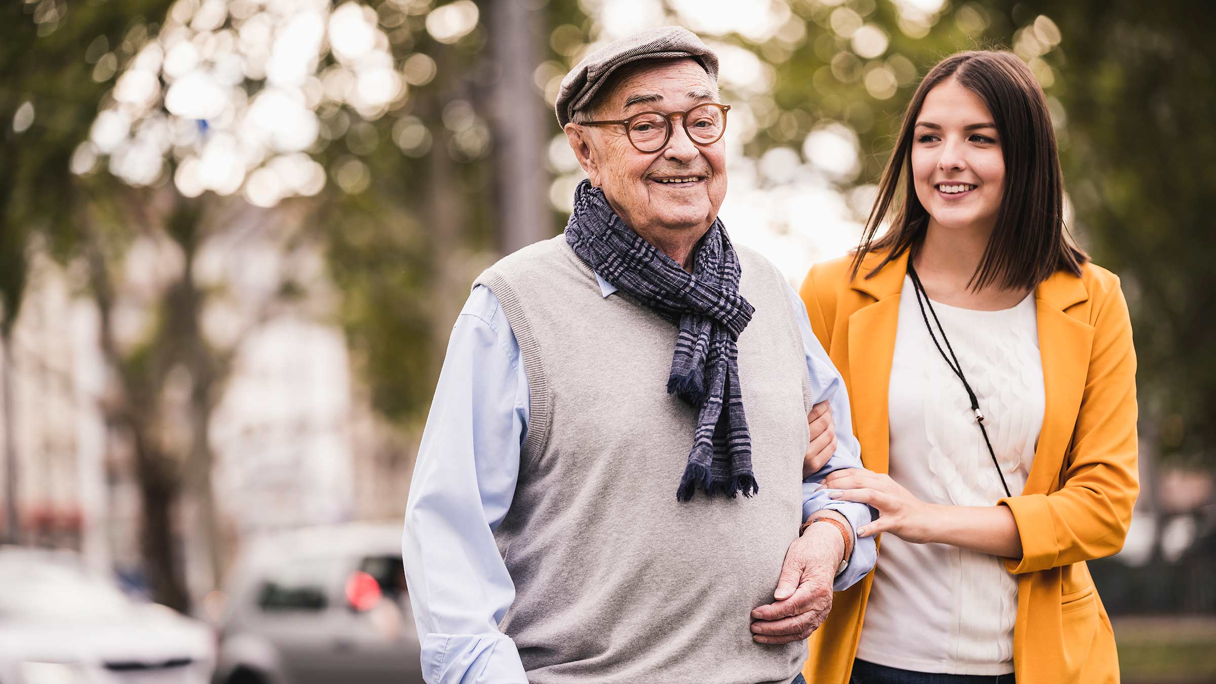 A senior man walking with his adult granddaughter holding onto his arm