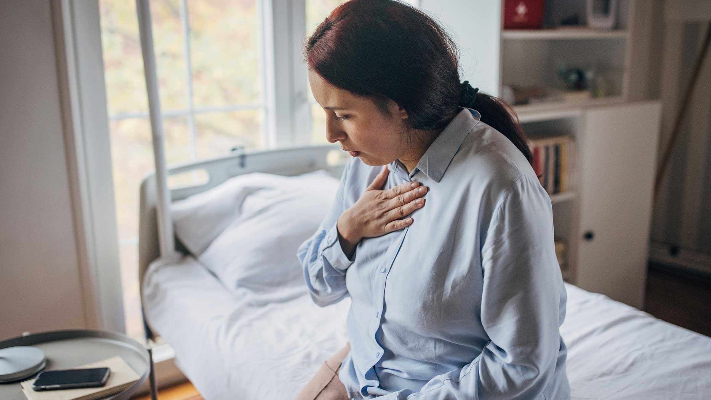 Woman feeling chest pain while sitting on bed