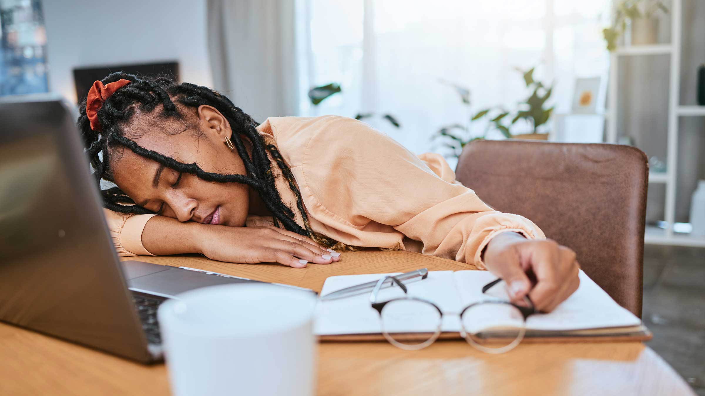 Woman asleep at her desk in front of her computer, holding her glasses