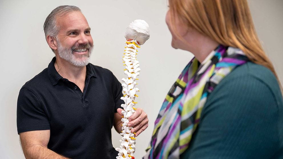 A woman speaking with a chiropractor whose holding a model of the spine