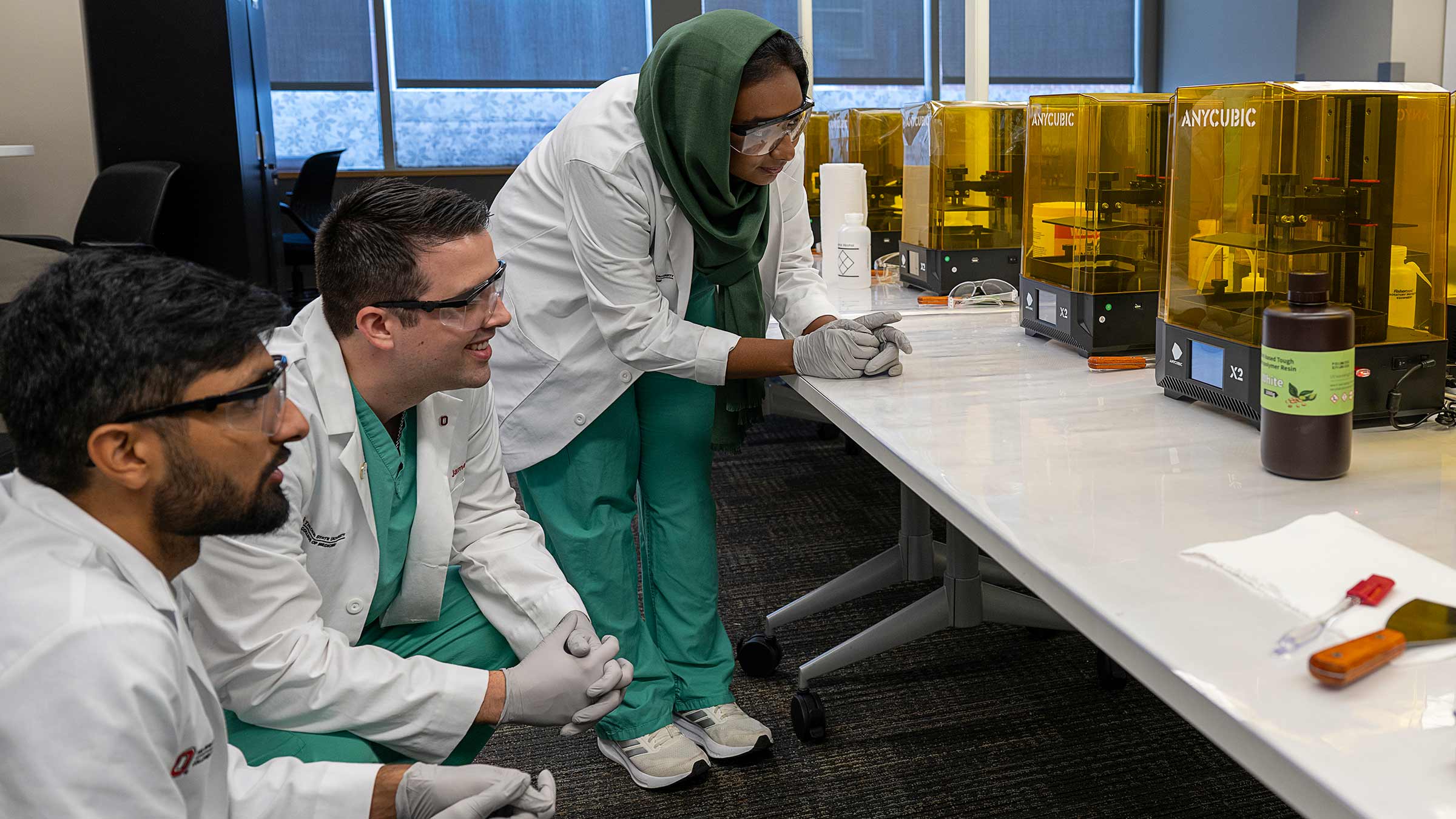 Three medical students observing a 3D printer creating a model