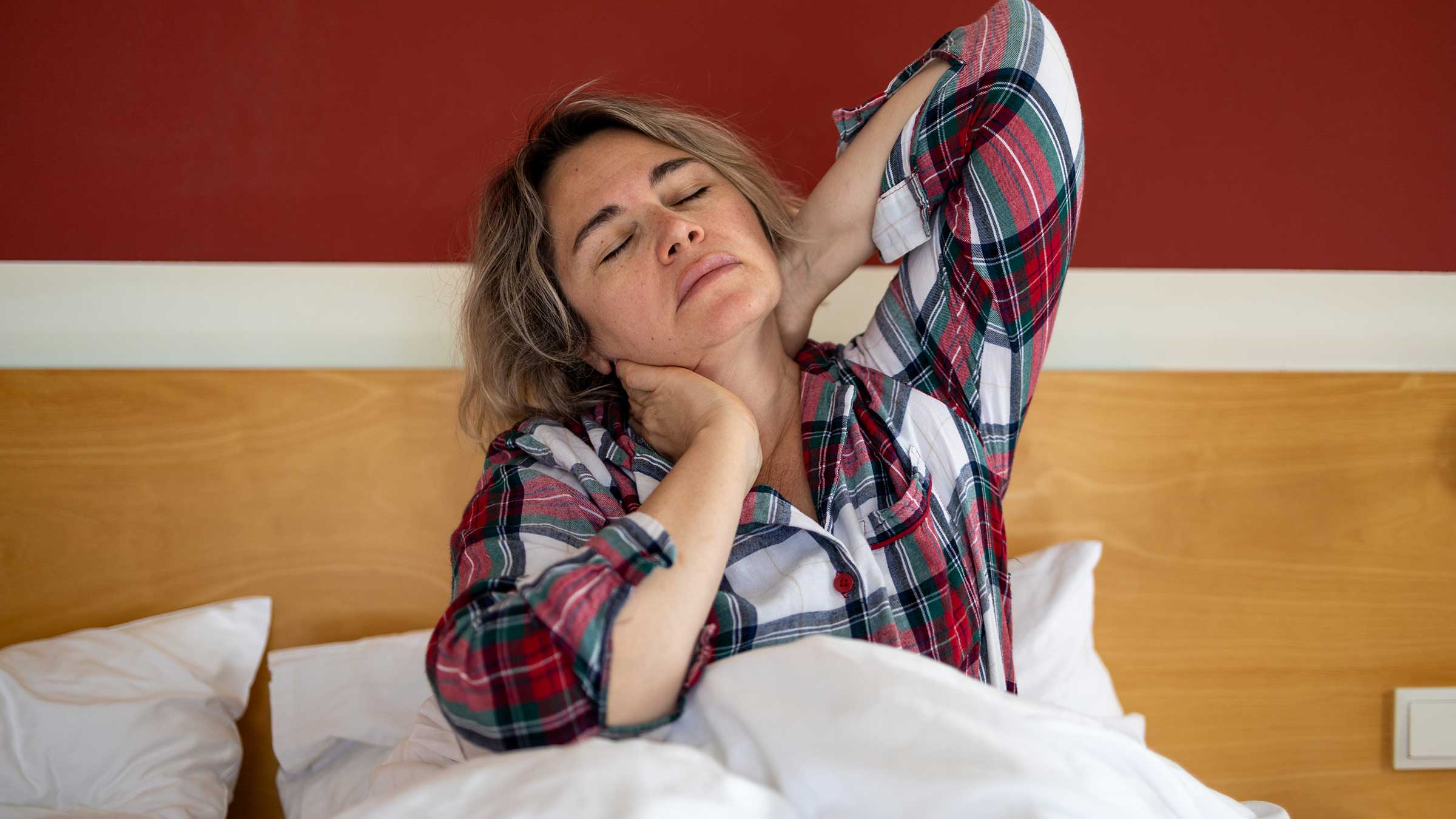 A woman sitting up in bed stretching her neck and arms