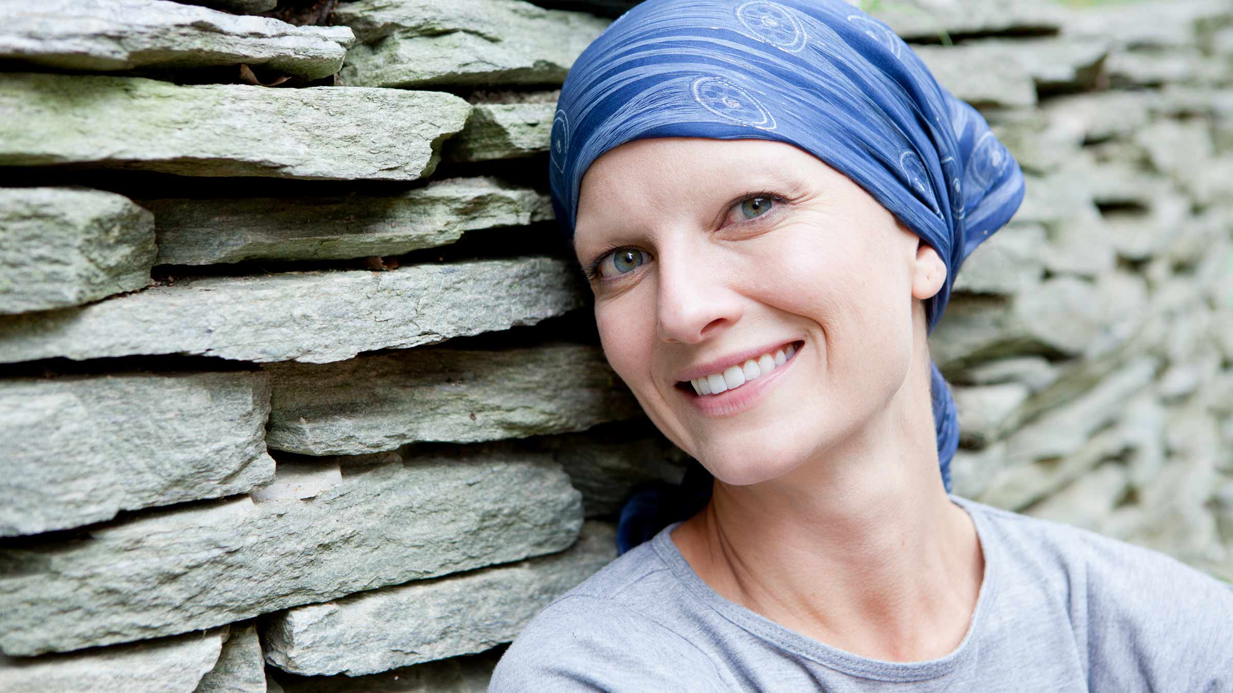 A smiling woman with cancer and wearing a scarf covering her head