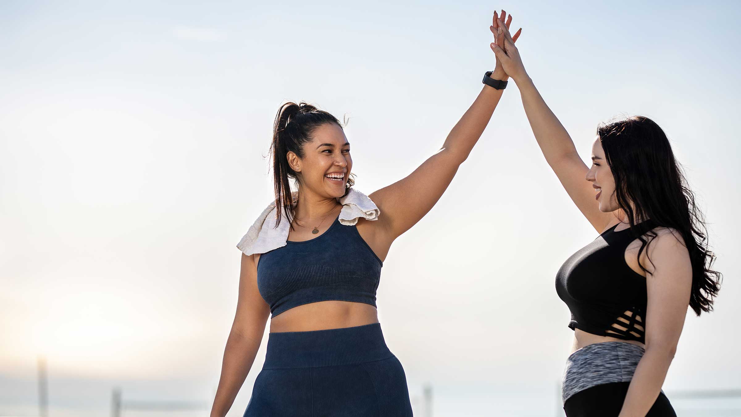 Two smiling women are wearing workout clothing and high-five