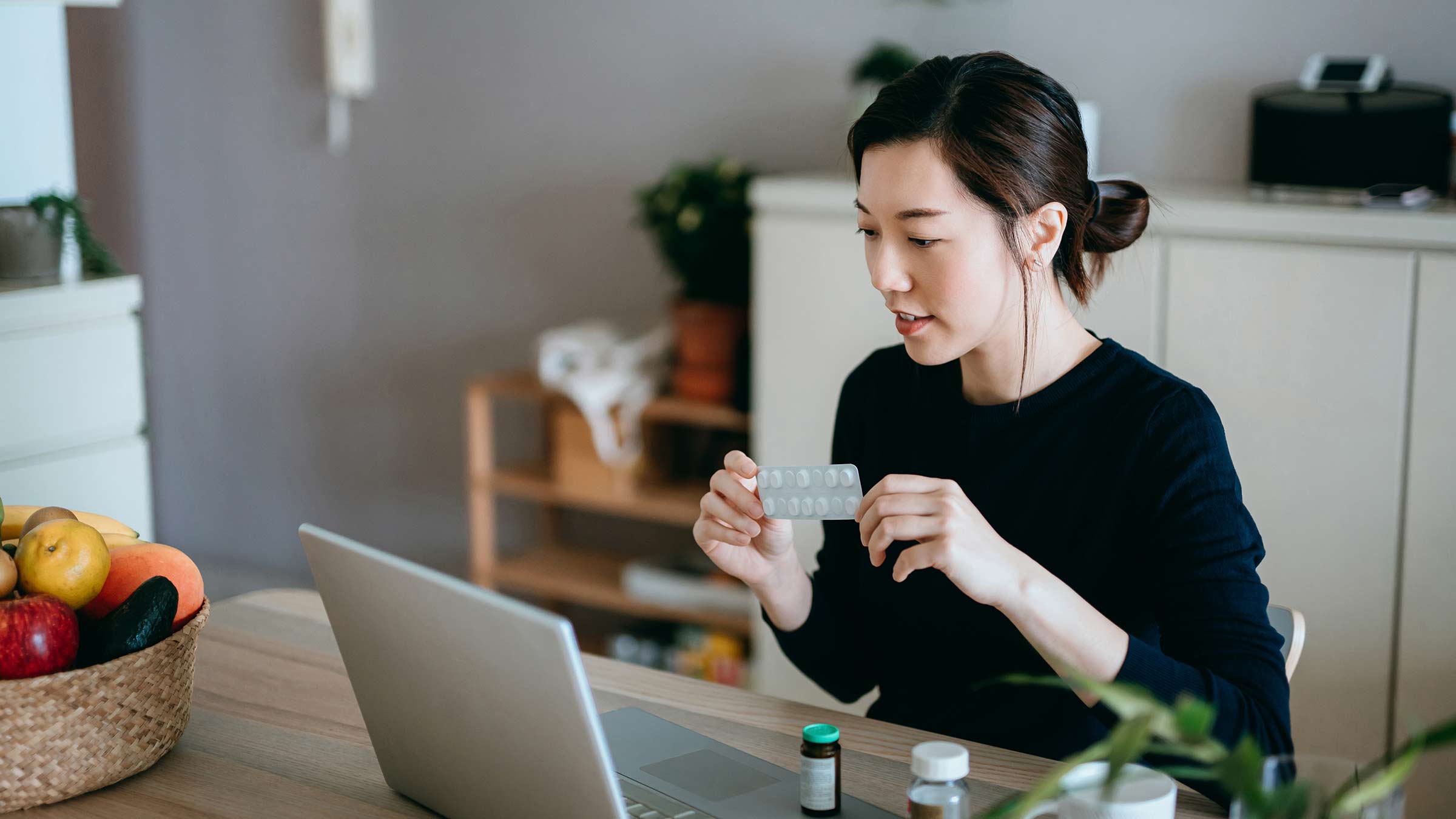 A young woman sitting at a kitchen on a tele-health call on a laptop
