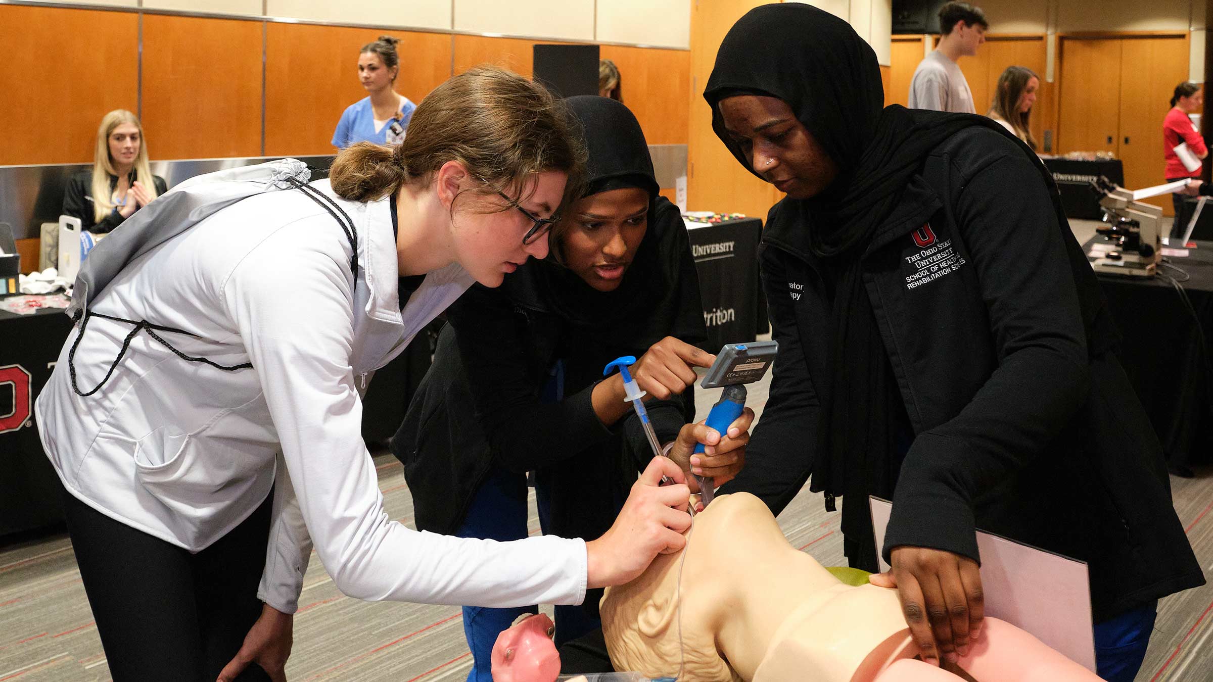 Two healthcare professionals demonstrating respiratory therapy on a mannequin for a prospective student