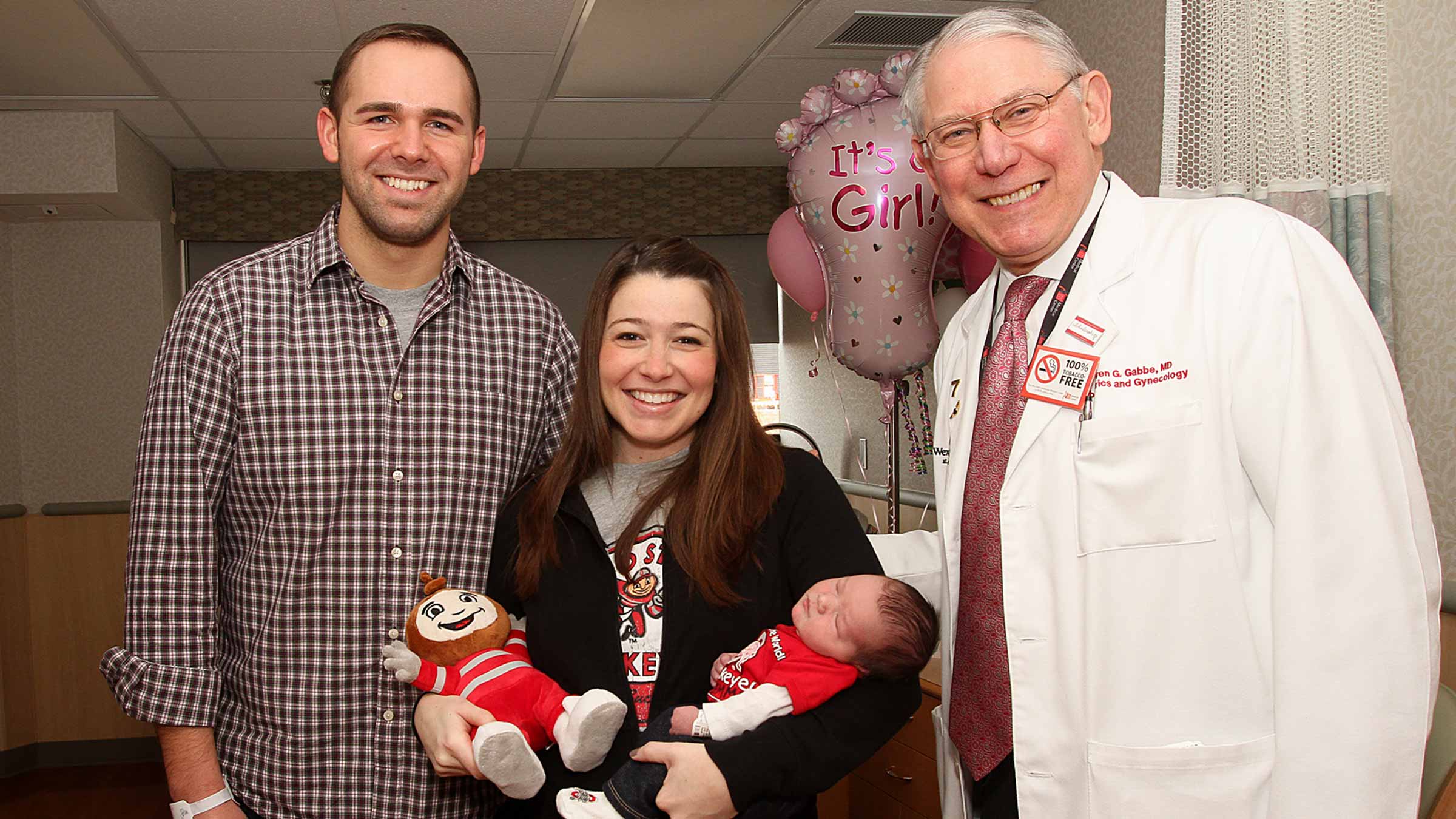 Steven Gabbe, MD, standing with his patient, her partner, and her newborn