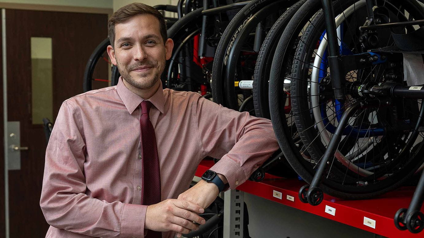Dr. Timothy Hake leans against a rack of wheelchairs and assistive equipment