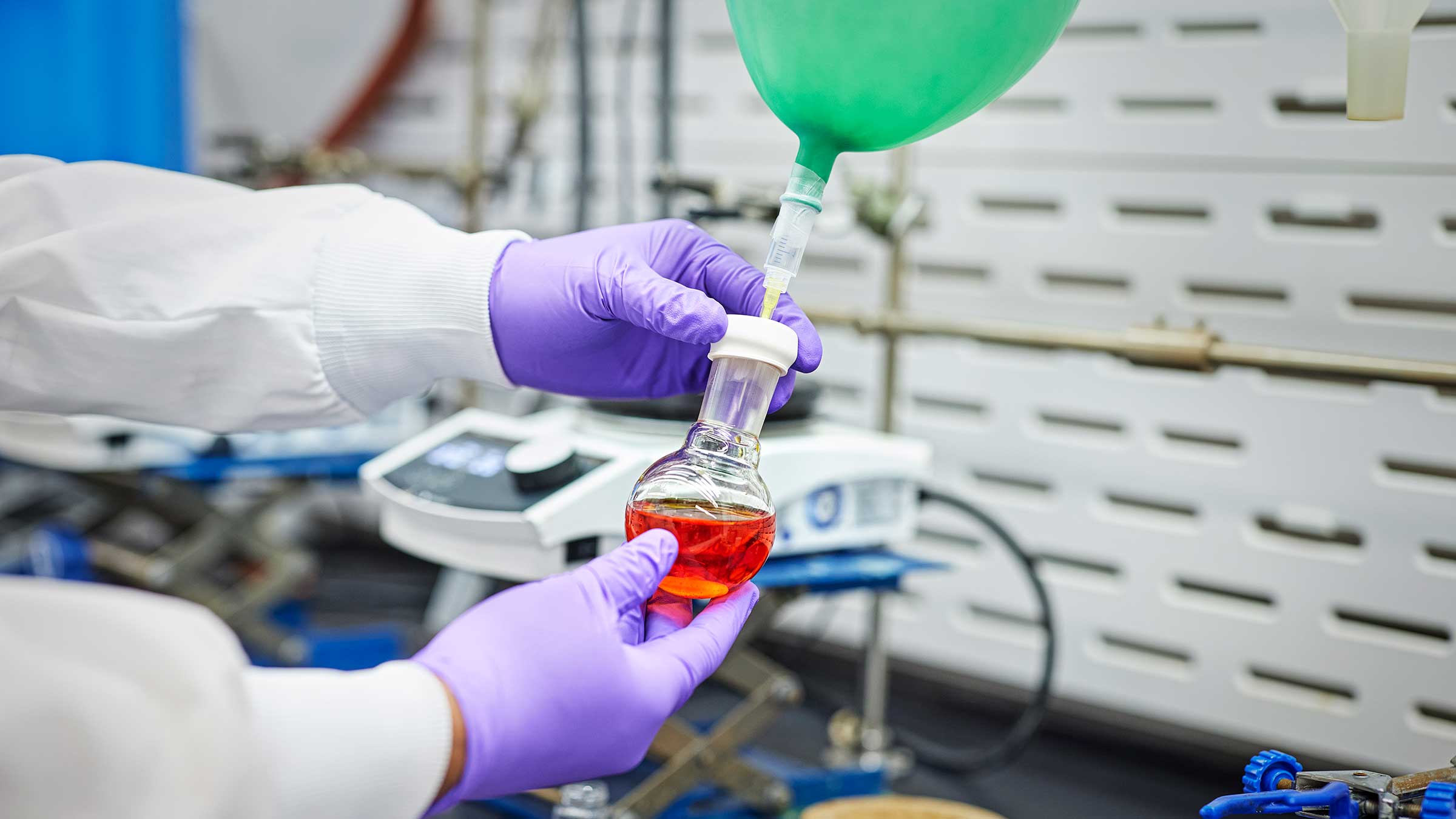 A scientist in a lab holding a round-bottom flask containing red liquid