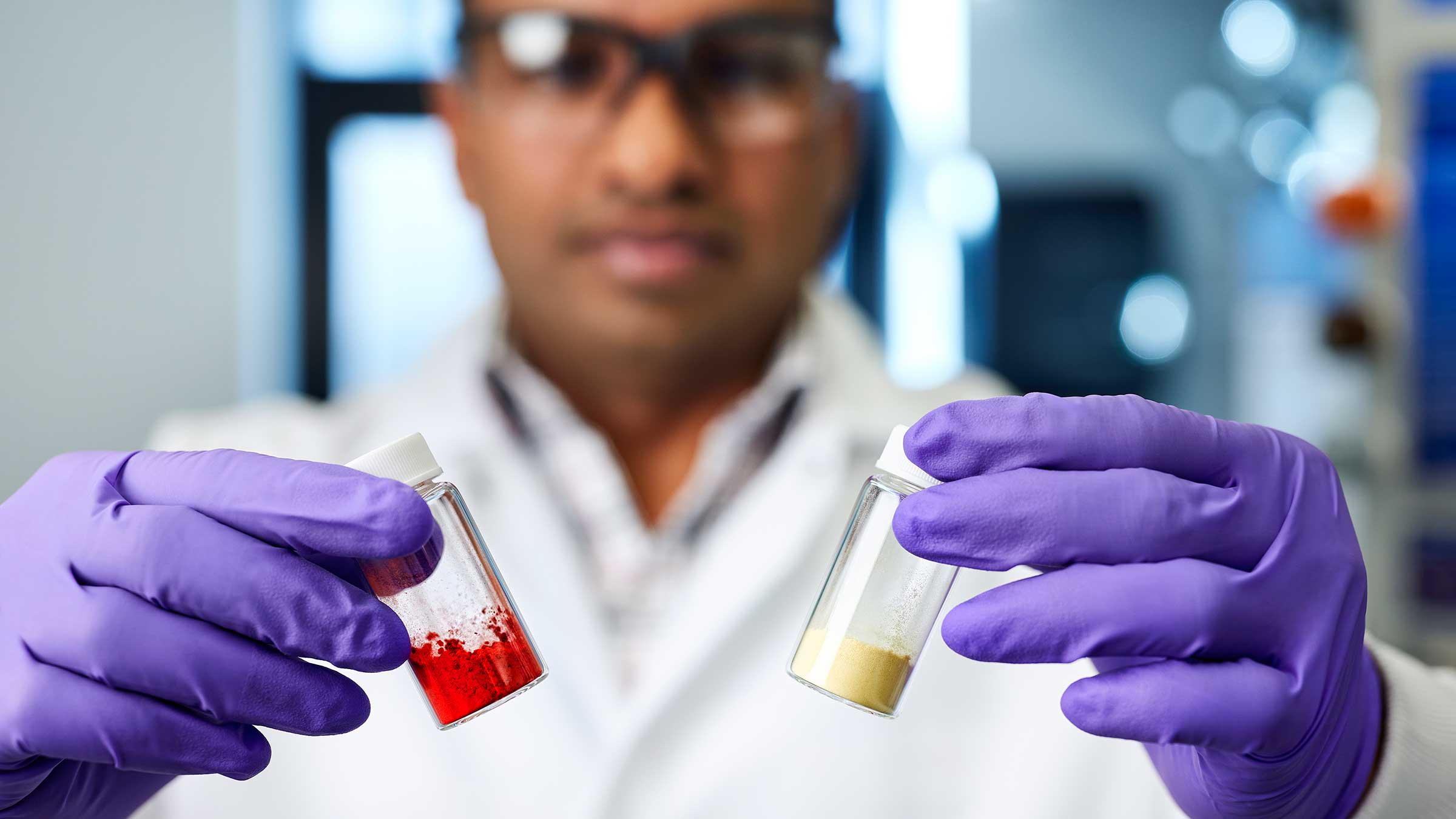 A scientist holding two vials—one containing red powder and the other yellow powder