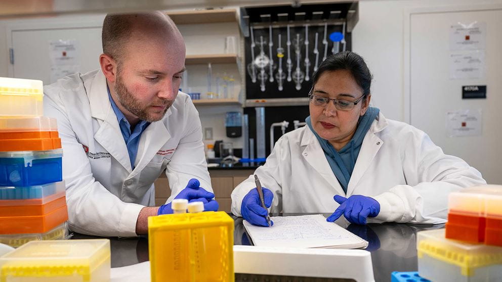 Dr. Thomas Mendel reviewing notes with a colleague in a lab setting