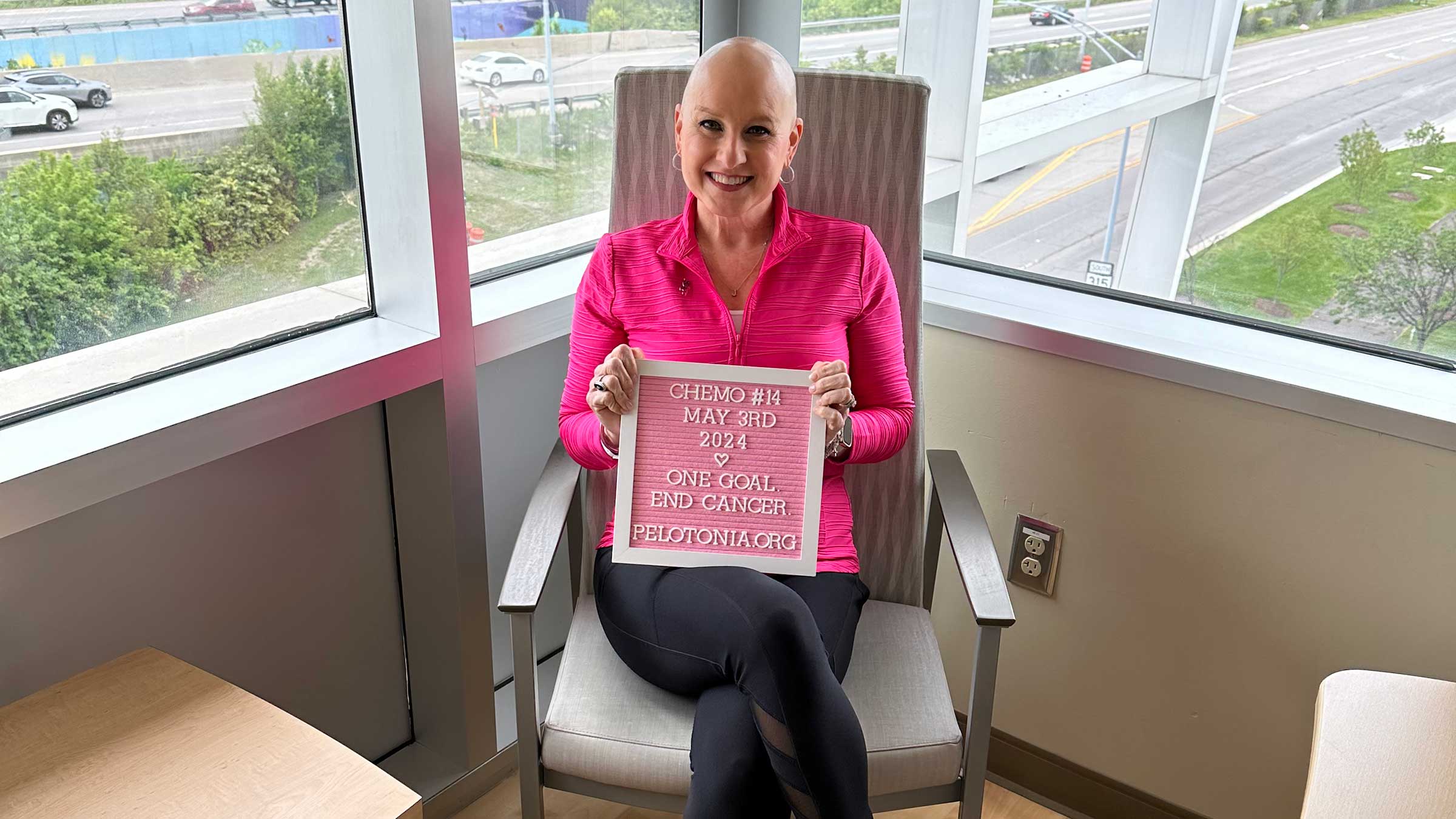 Julie Kriss holding a sign: "Chemo #14, May 3rd, 2024. One goal. End Cancer. Pelotoninia.org"