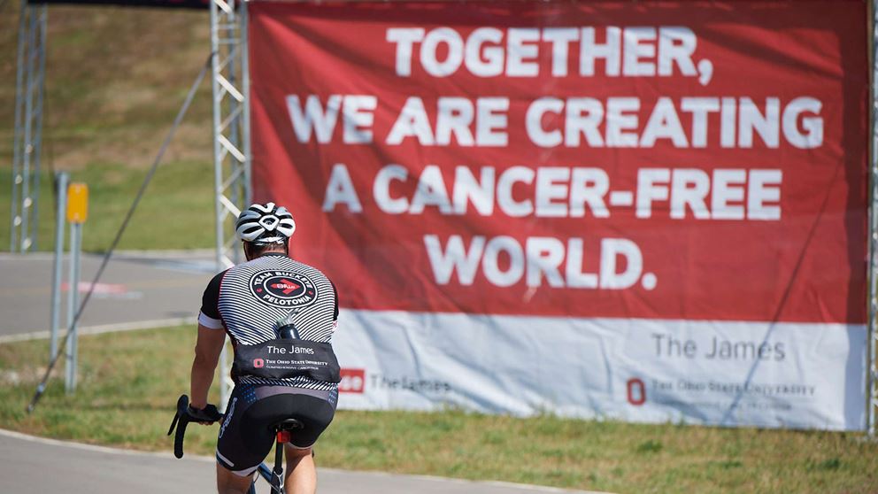 The rider biking past the banner: "Together, we are creating a cancer-free world".
