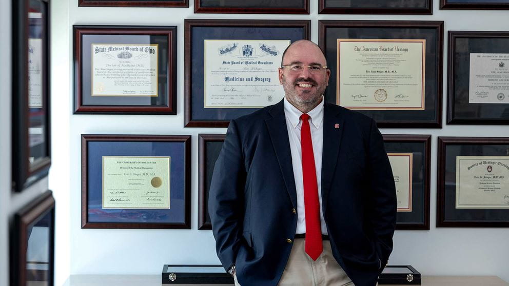Dr. Singer in front of a wall with multiple framed certificates and diploma