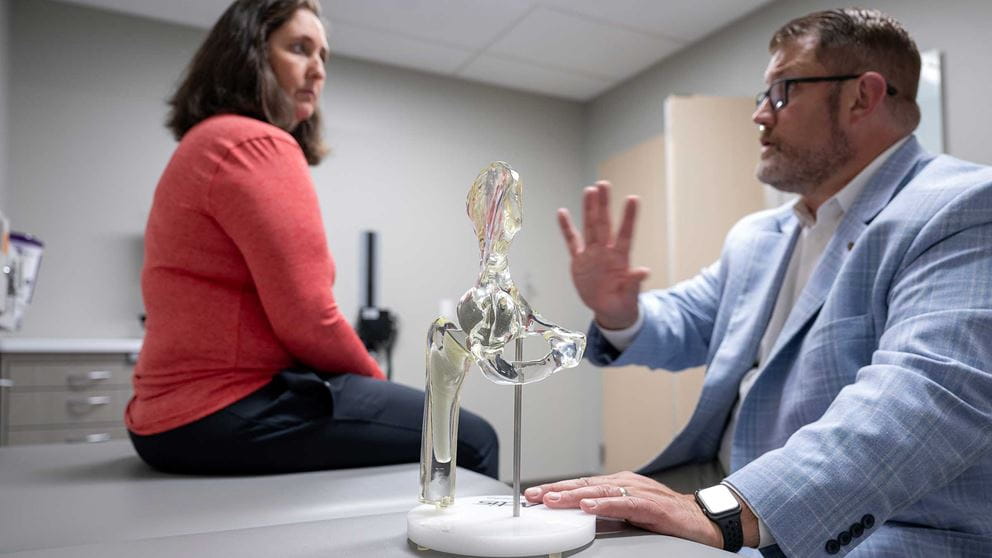 Doctor Matthew Beal shows a hip replacement model to a patient