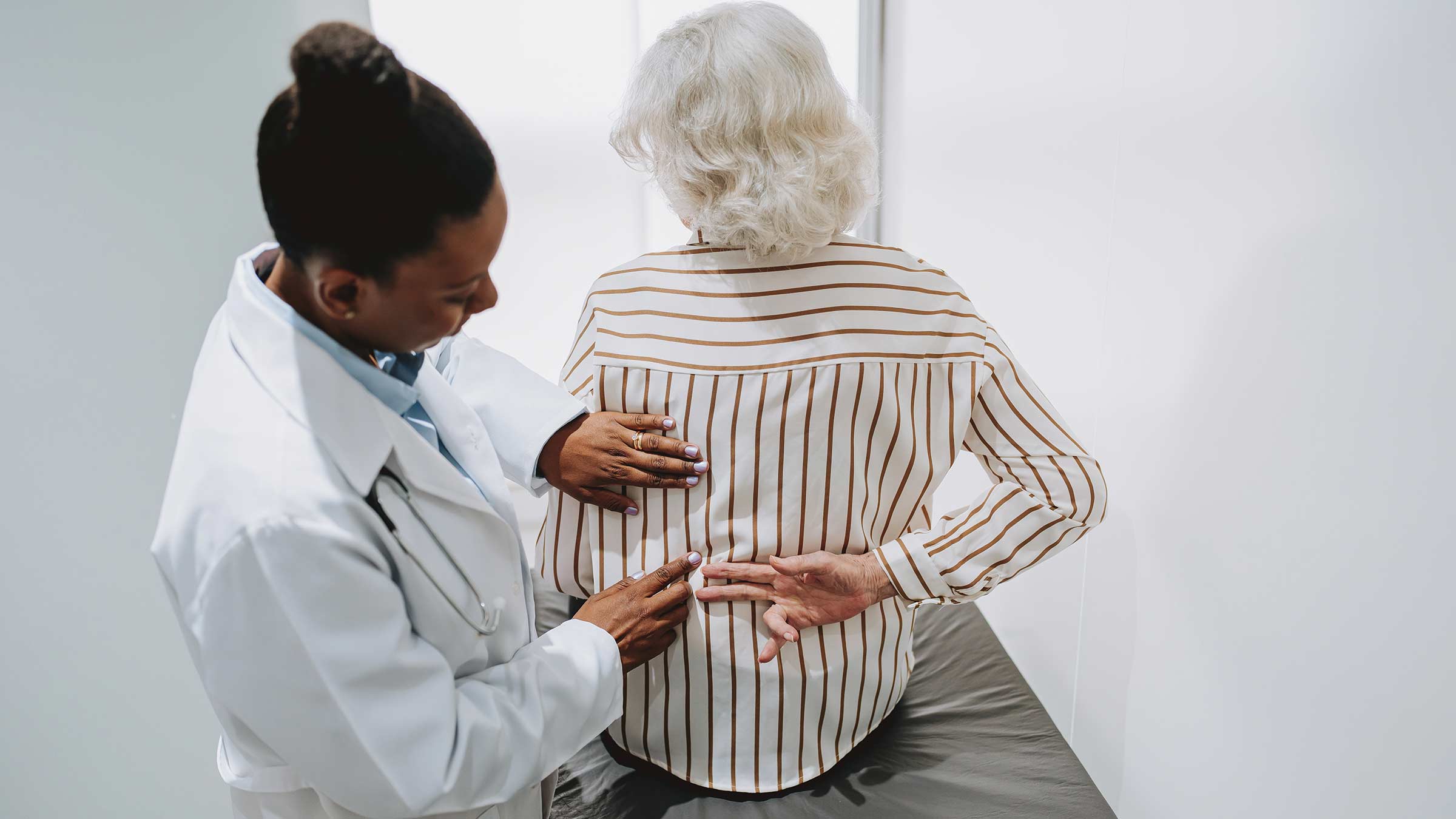 A doctor examines a patient’s back while the pain is being described and pointed out