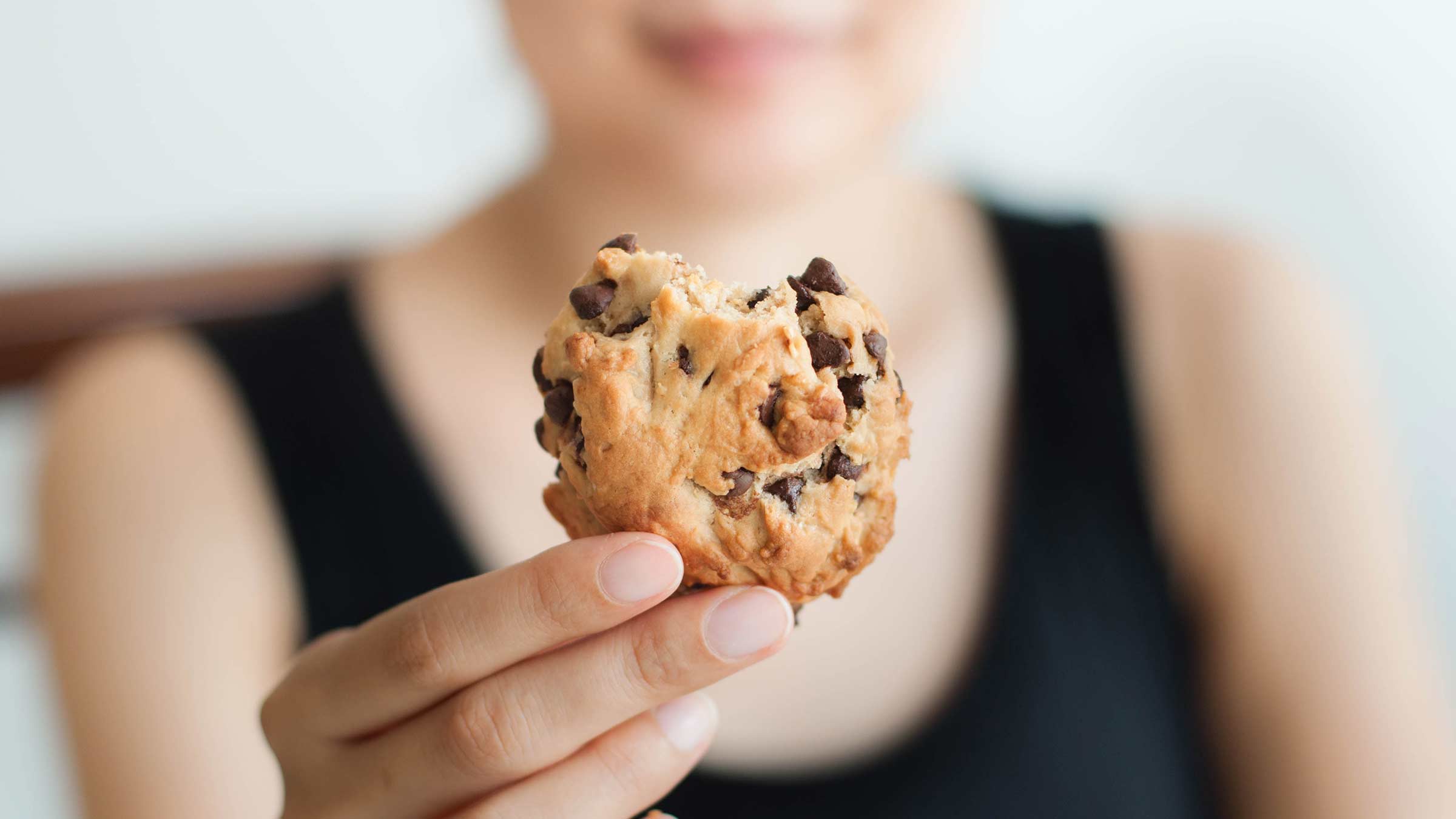A close-up image of a young woman holding up a cookie
