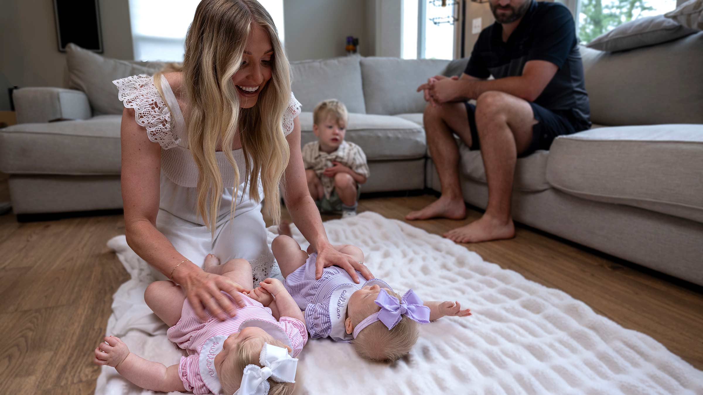 Madison Feinberg playing with her daughters on the floor with her husband and son on the background