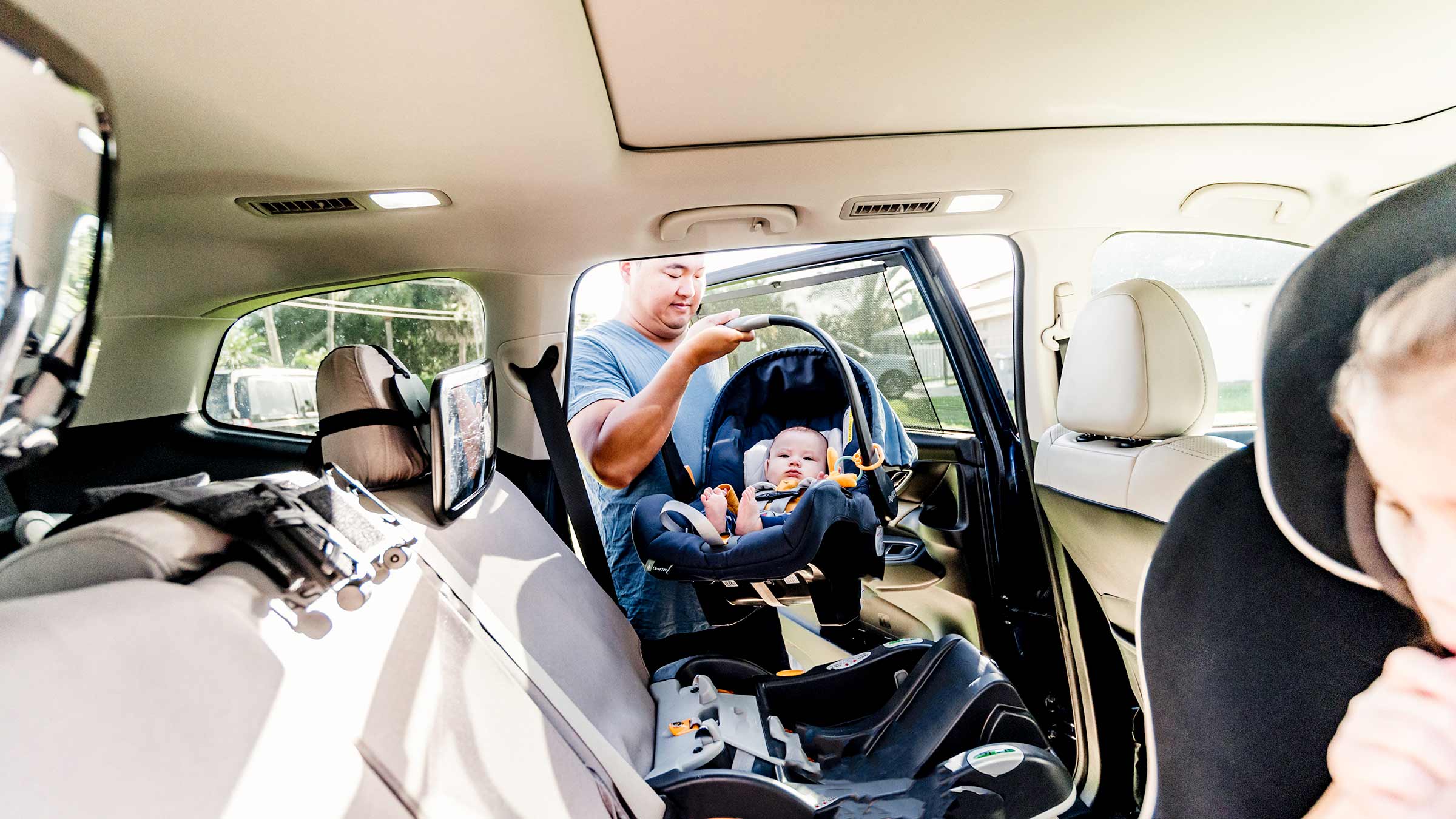 A parent putting their infant and infant car seat into the back seat of the car