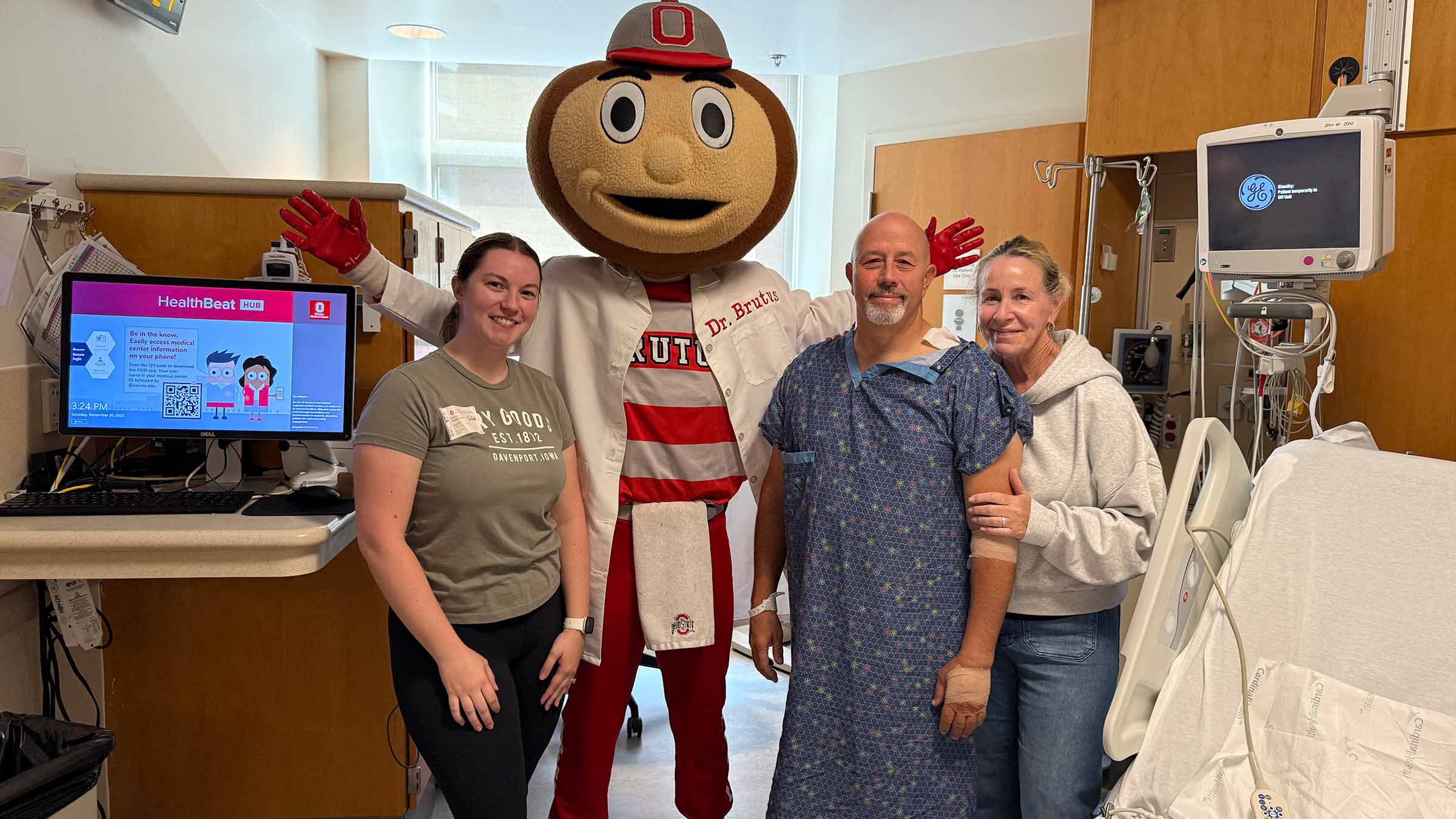 Carmen Zone in a patient room standing with his wife, daughter and Brutus Buckeye