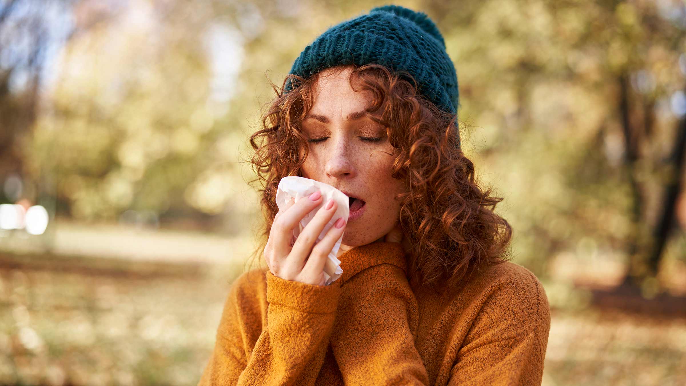 Person outside in the fall sneezing into a tissue