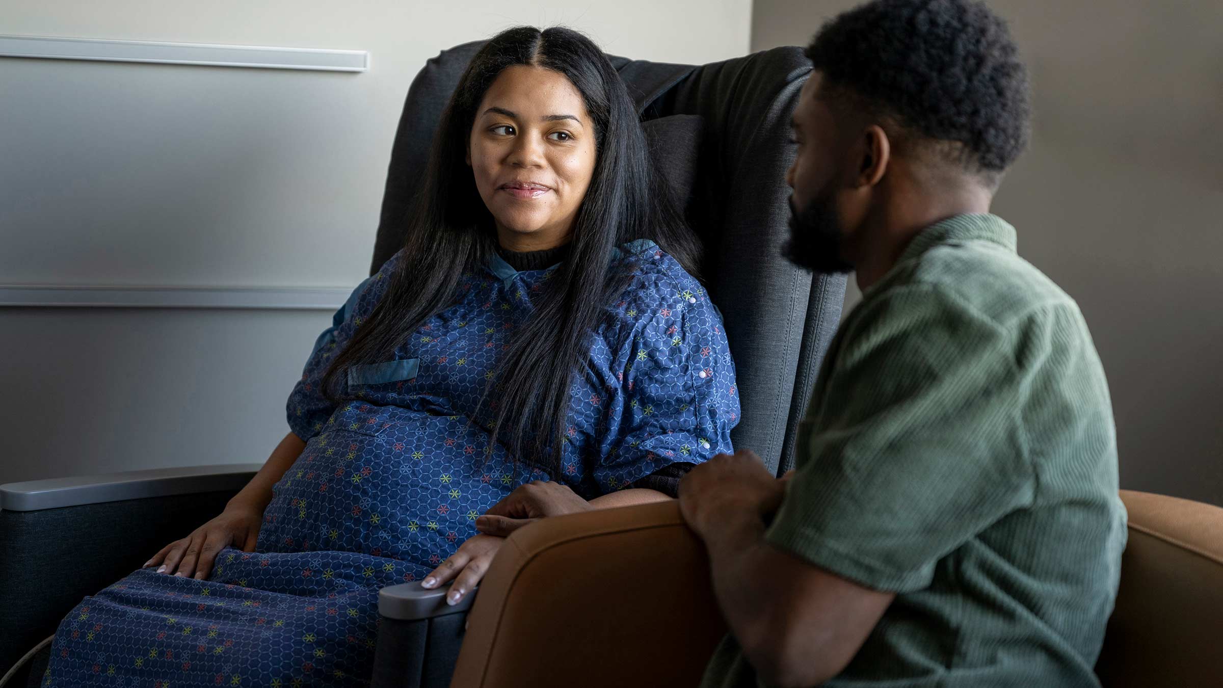 A pregnant woman in a medical gown looking at her partner in a private patient room