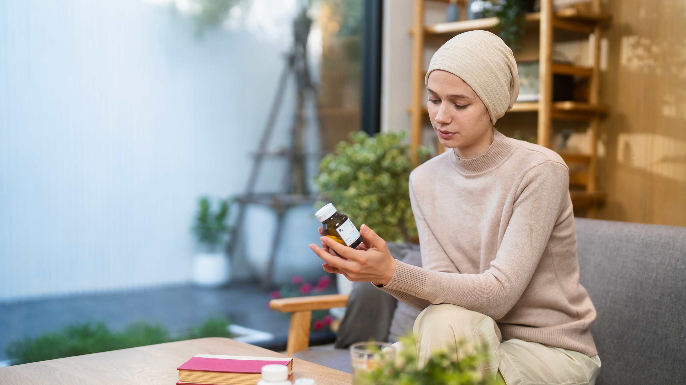 Woman with a hat covering her hair looking at a bottle of vitamins