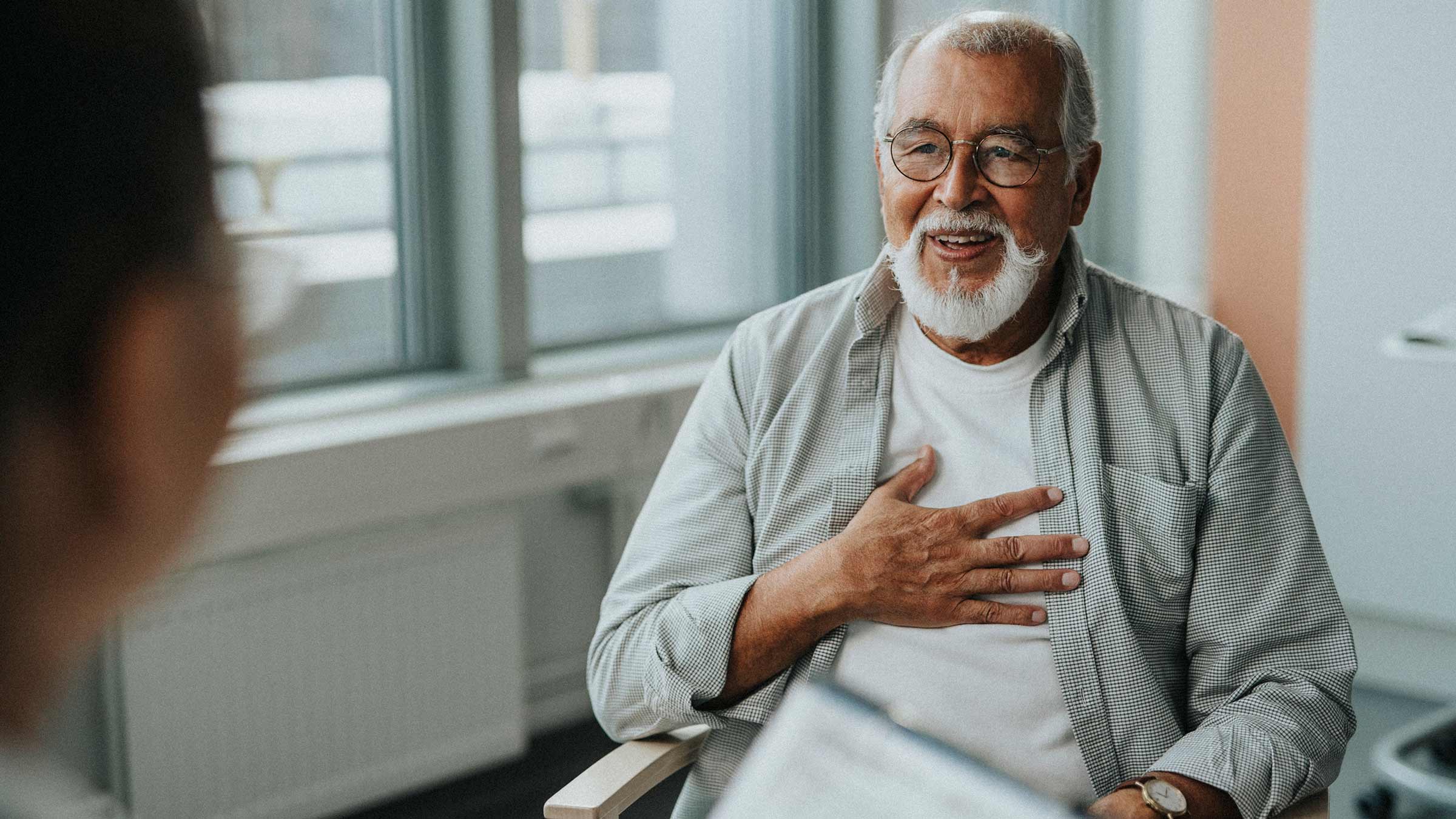 A senior male patient speaks with a physician with his hand on his chest