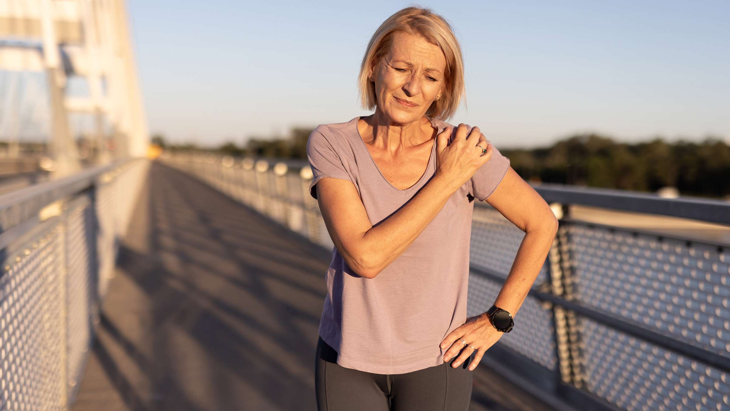 Older woman walking outside looking pained while holding her shoulder