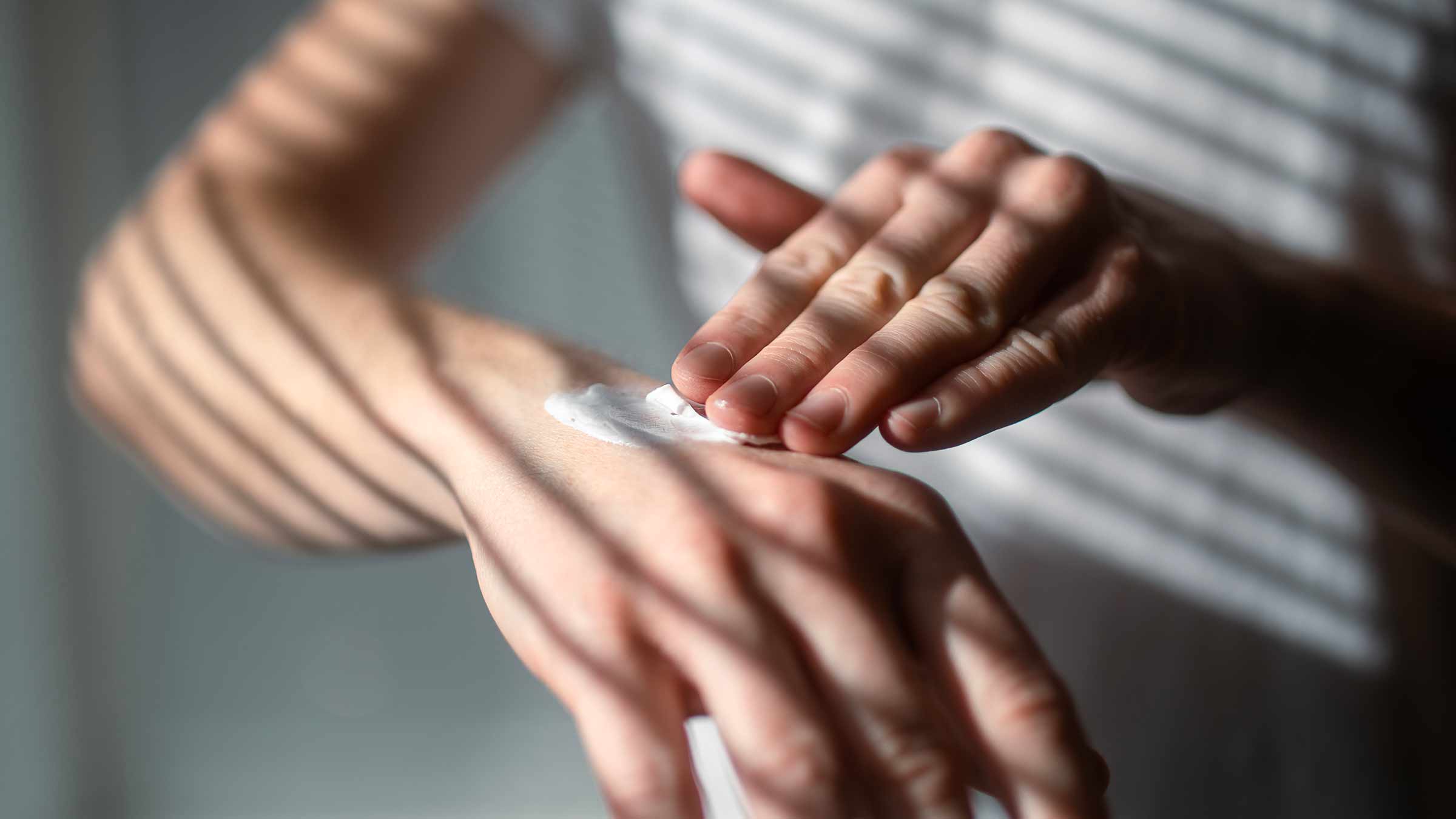 A close-up image of a person applying lotion to their hands