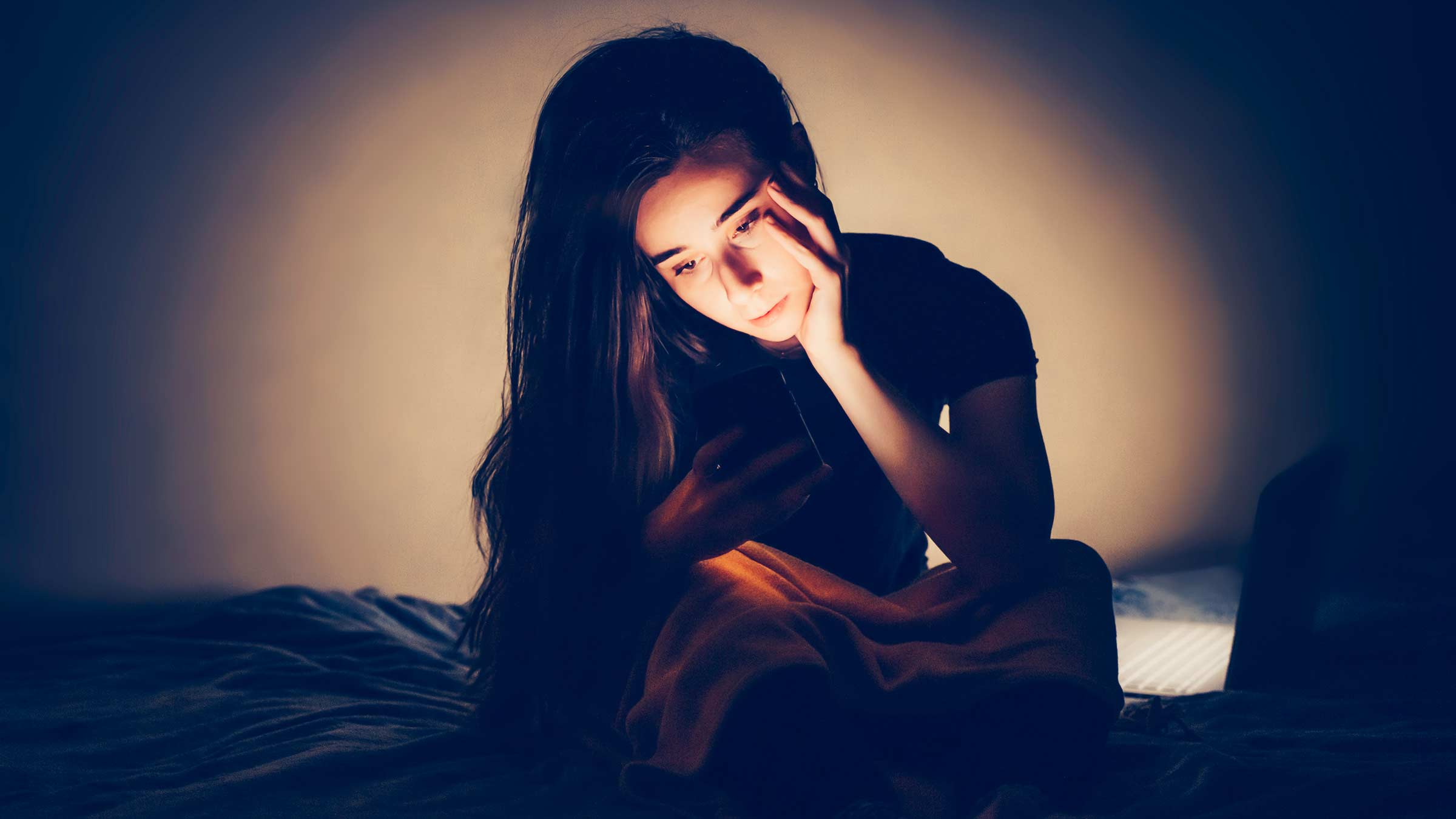 A young woman sitting in the dark, looking at her phone