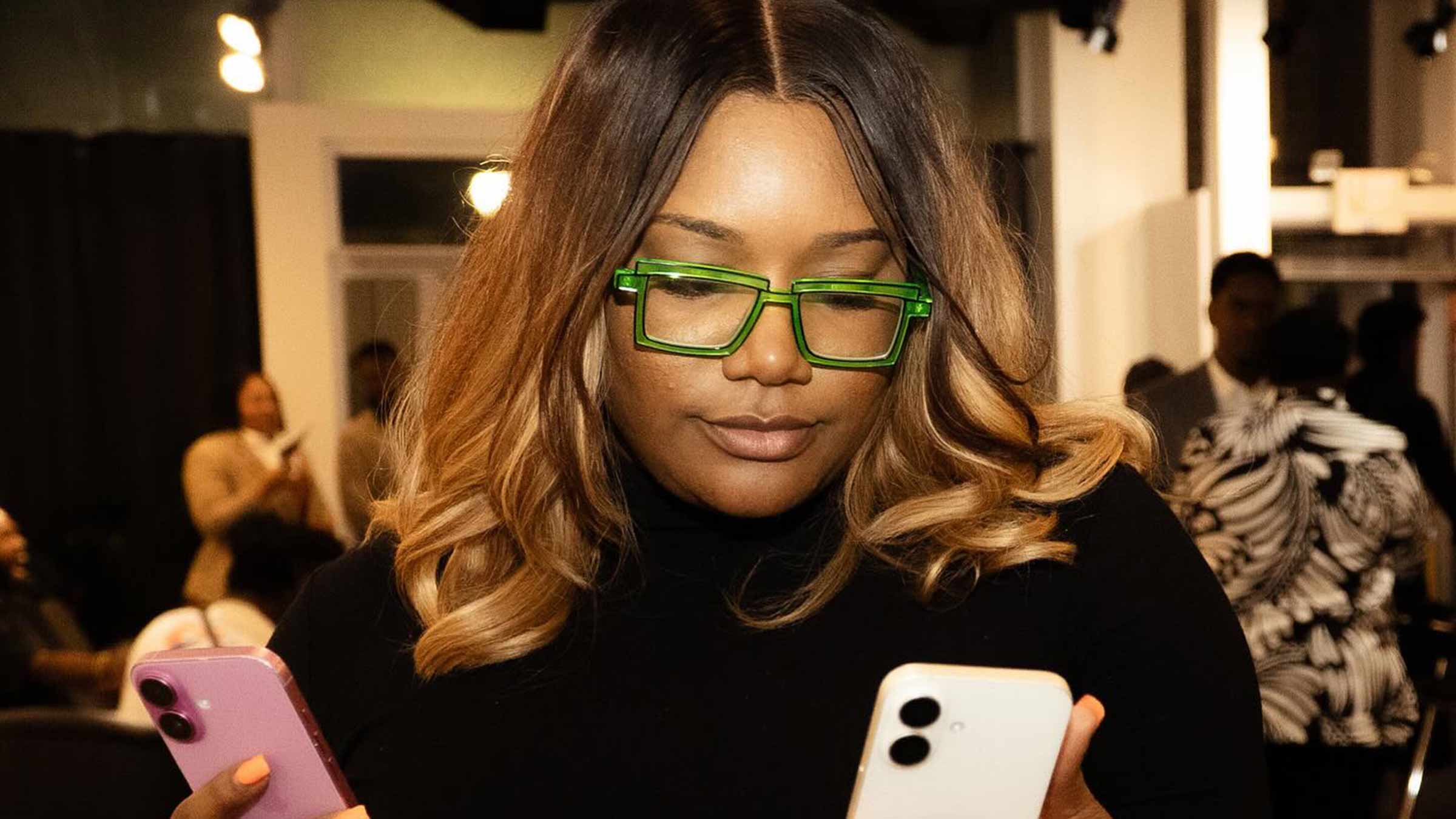 NaAsiaha Simon wearing bright green glasses and holding two phones in her hands