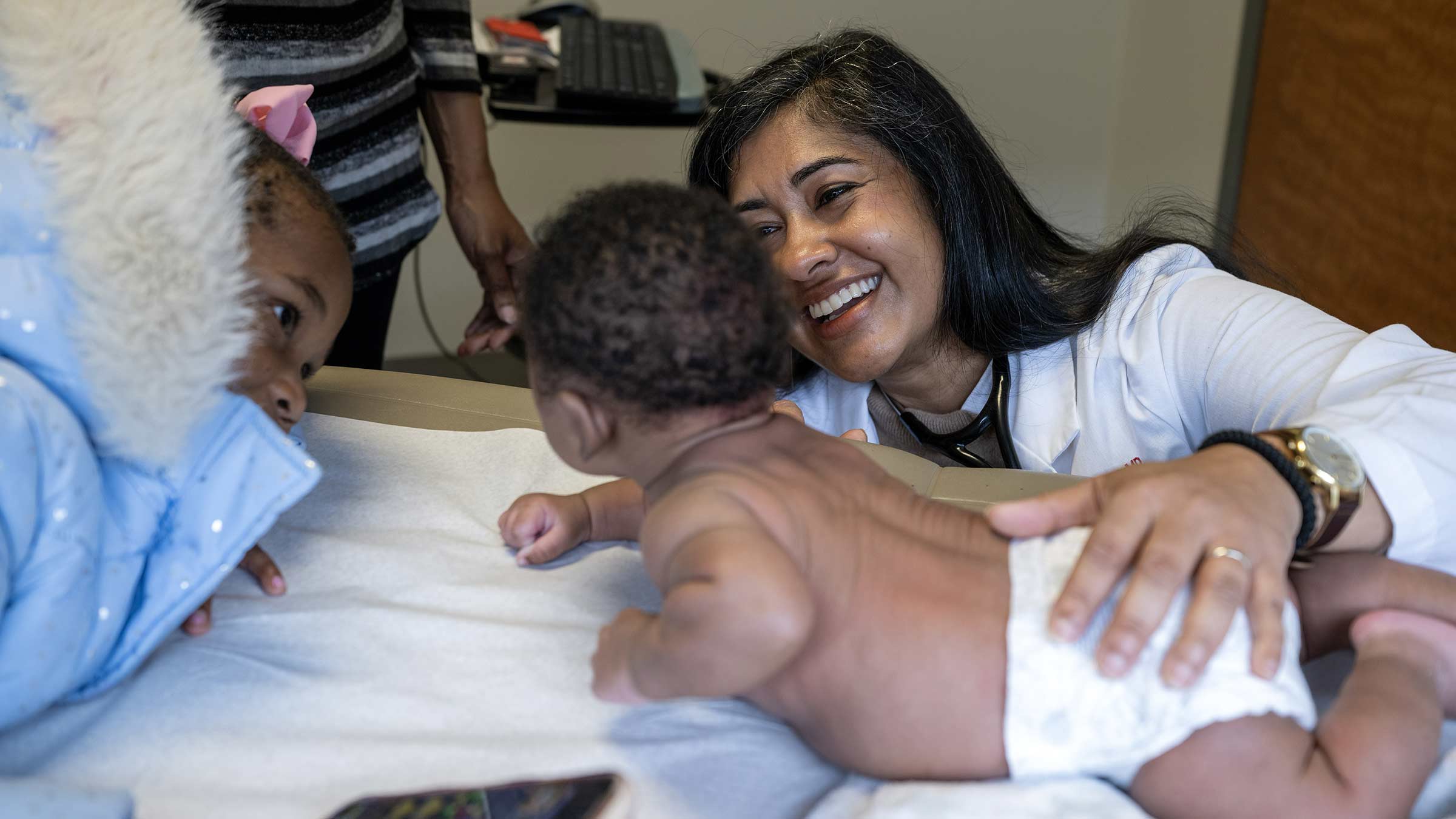Dr. Brill smiling at an infant while the infant’s sister looks on