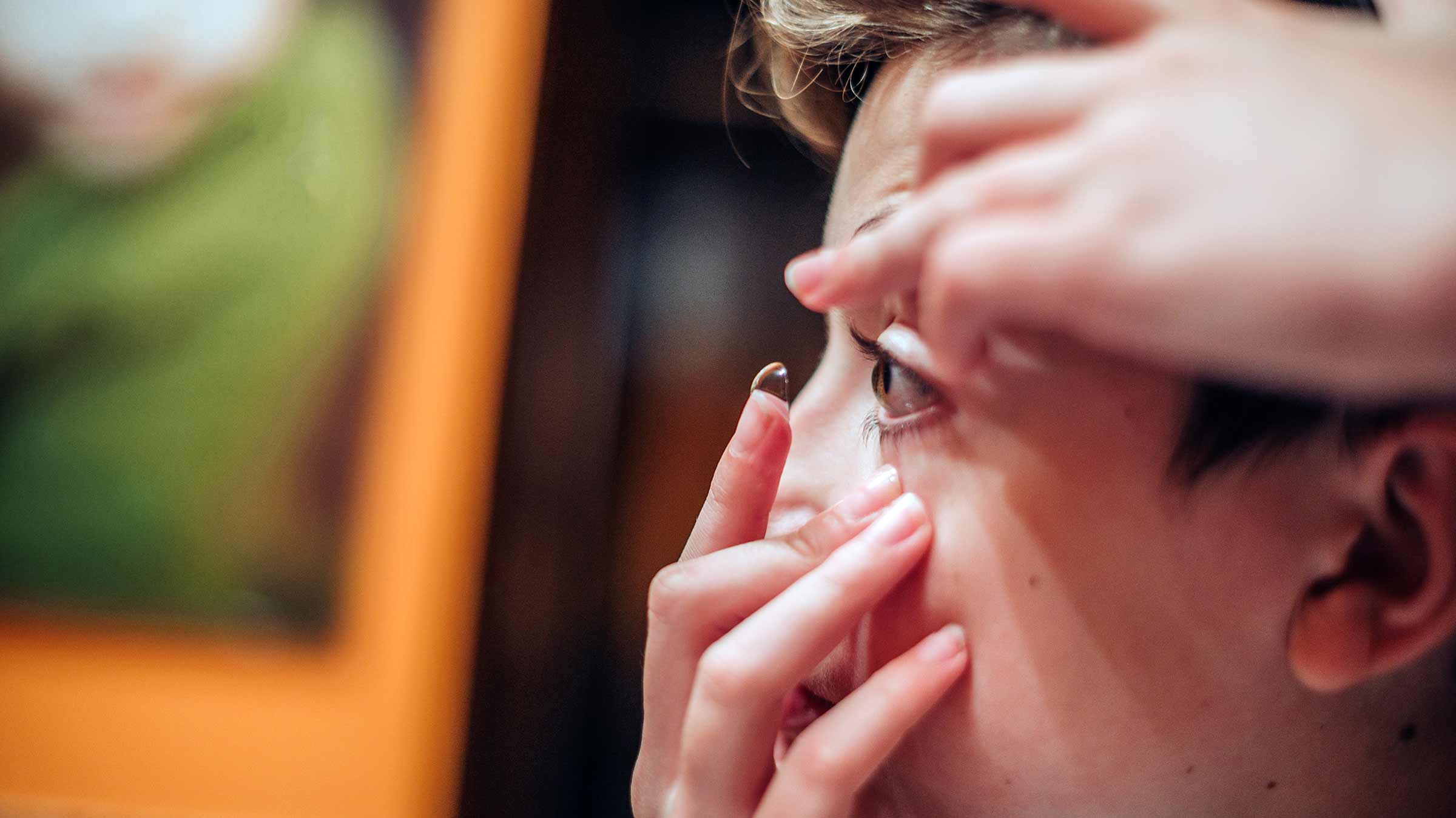 A preteen boy puts contact lenses into his eye