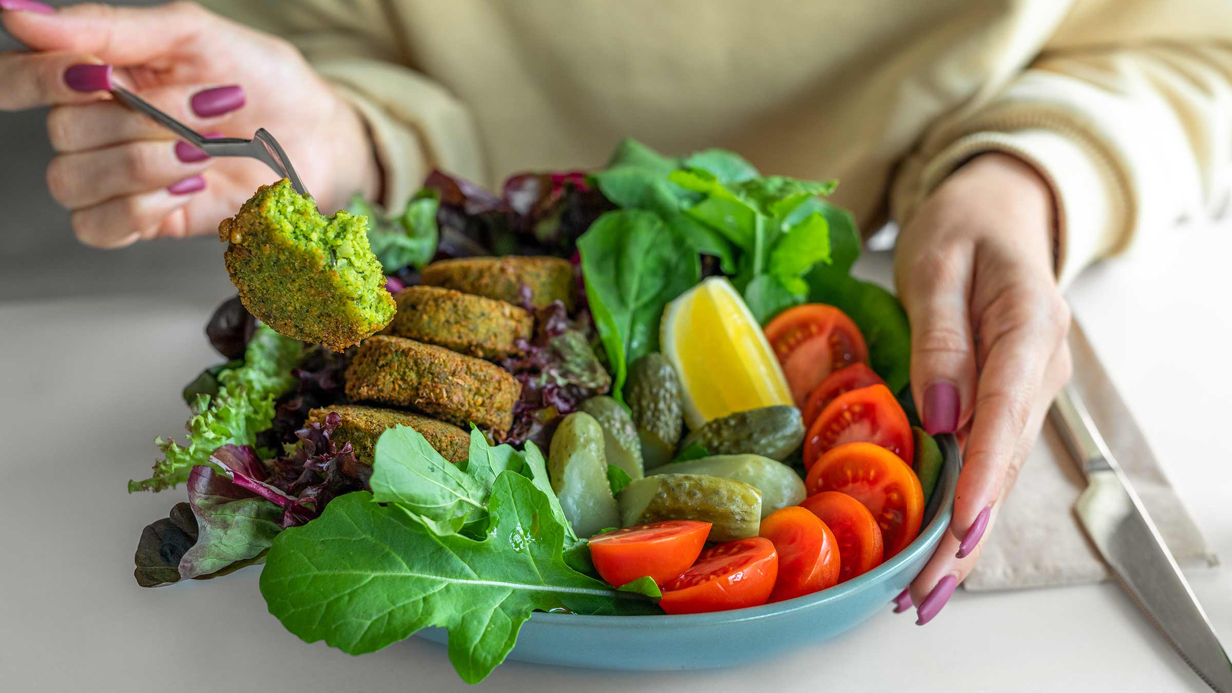 A close-up image of a woman holding a falafel salad with tomatoes, lemon and pickles