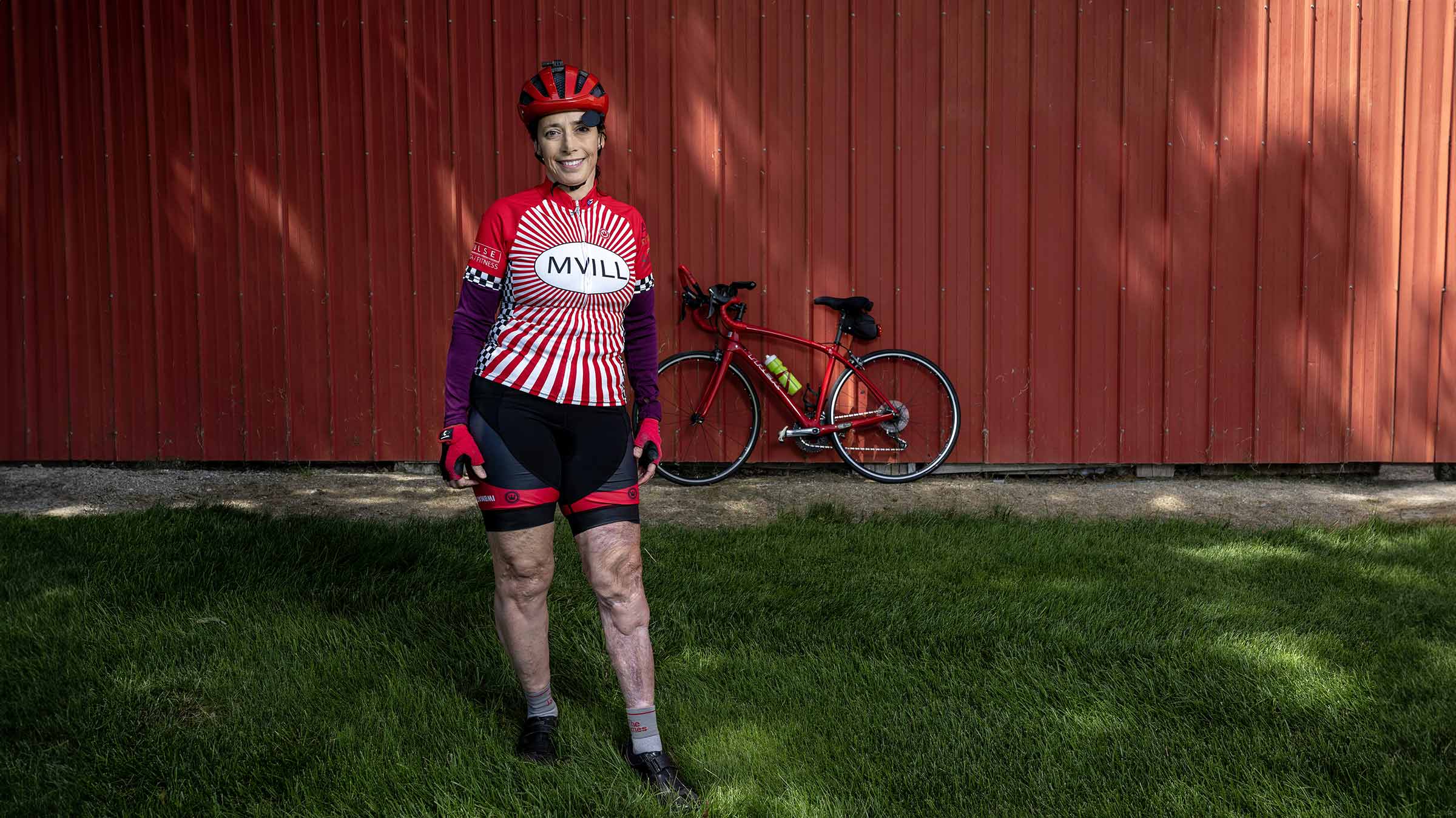 Mary Applegate wearing cyclist jersey and shorts with her bike leaning on a barn on the background