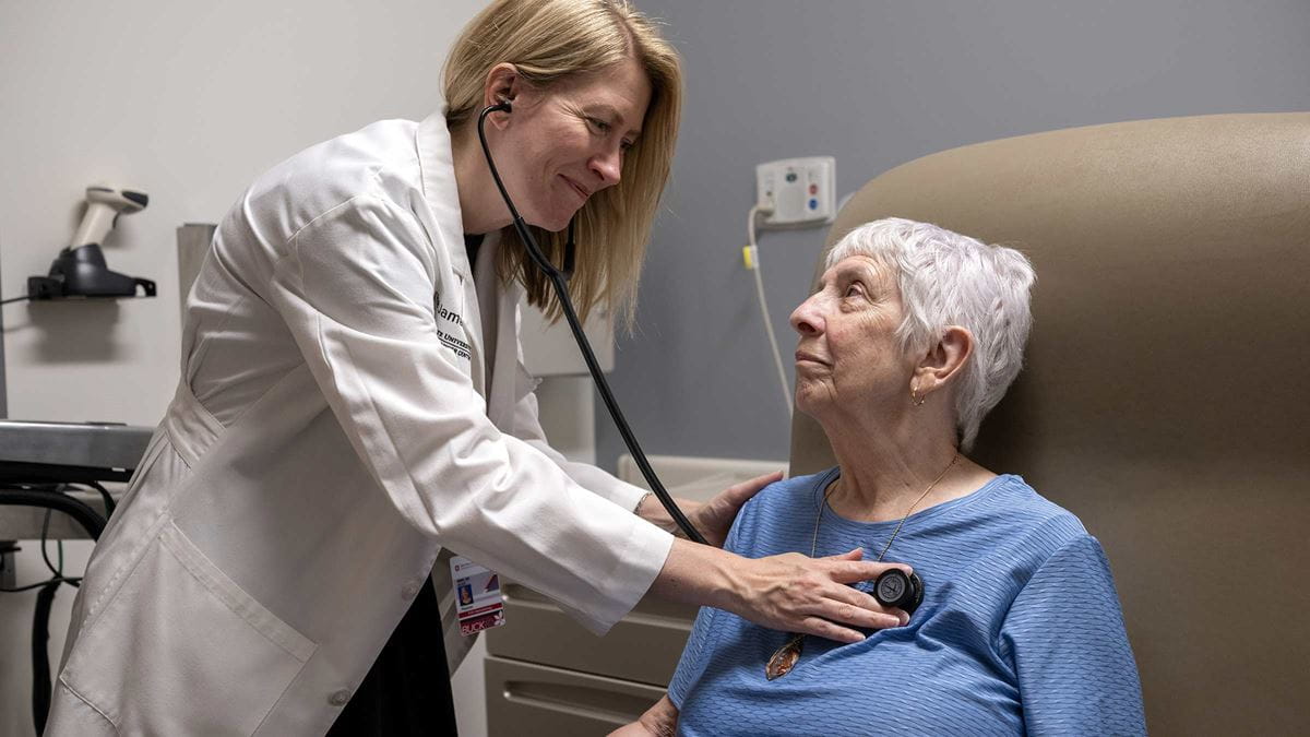 Alice Mims, MD, listening to a patient’s heart in an exam room