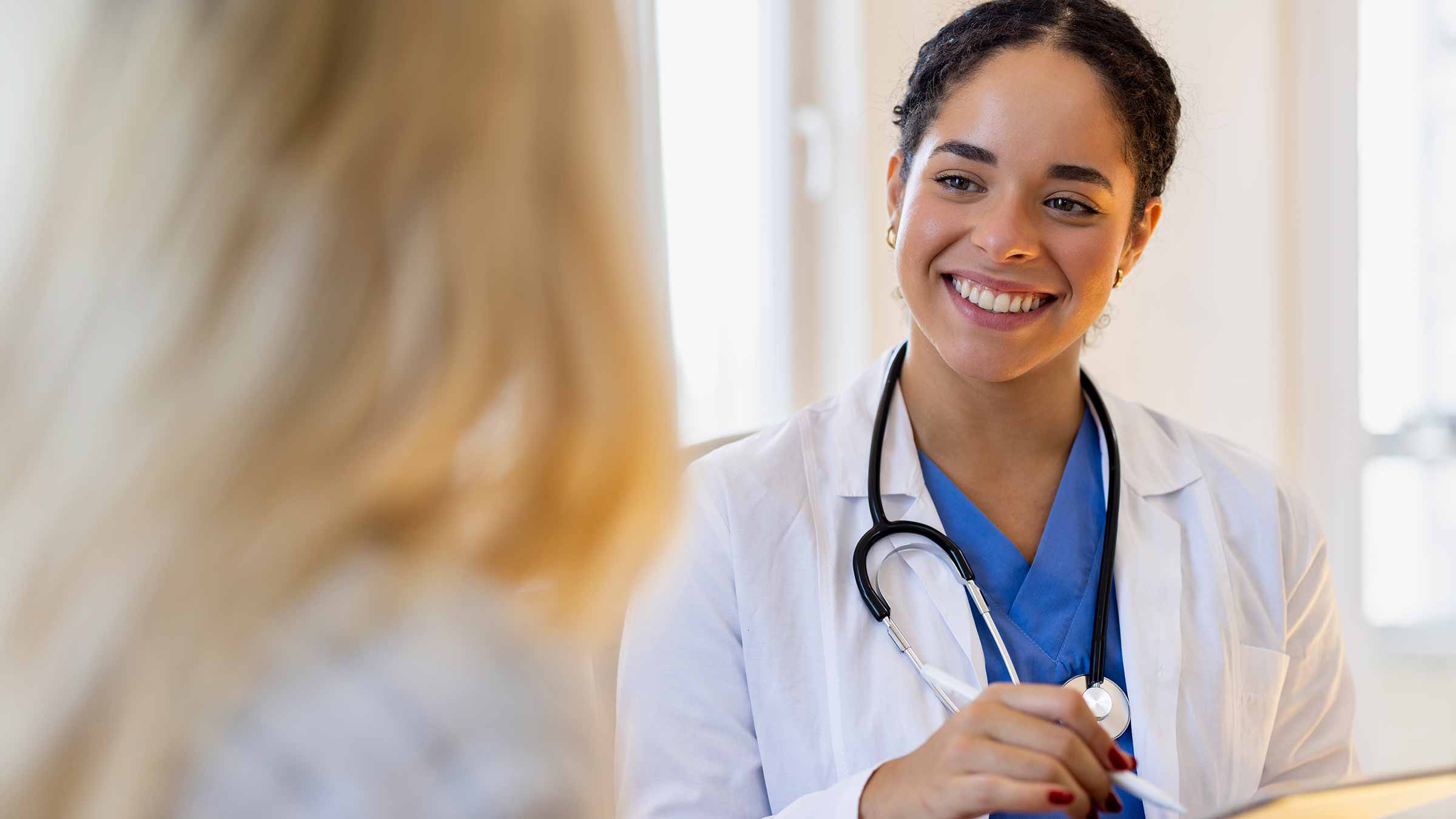 Smiling female physician holds a tablet while talking to a woman patient